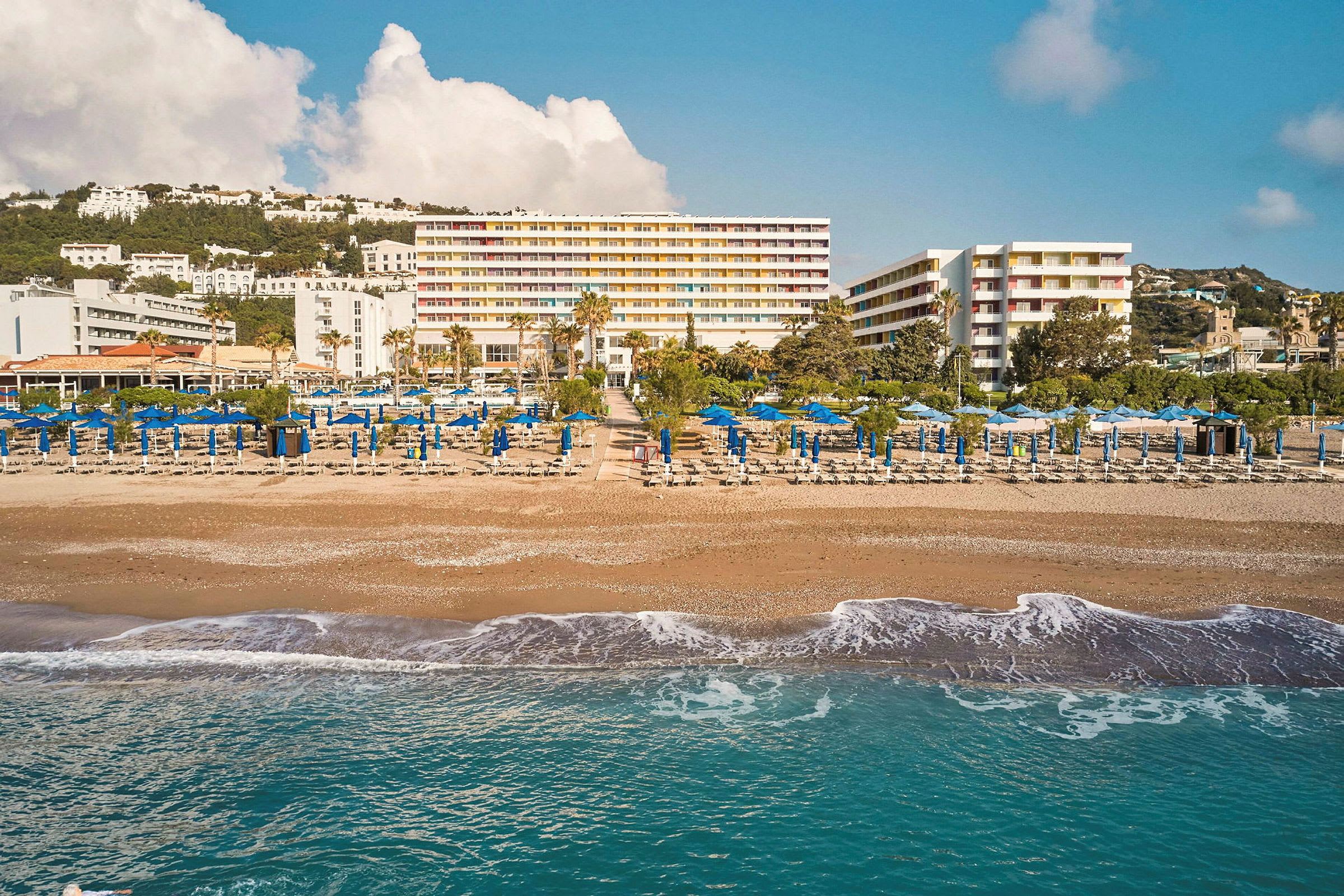 Strand med solstolar och parasoller framför ett hotell. (AI-genererad text)