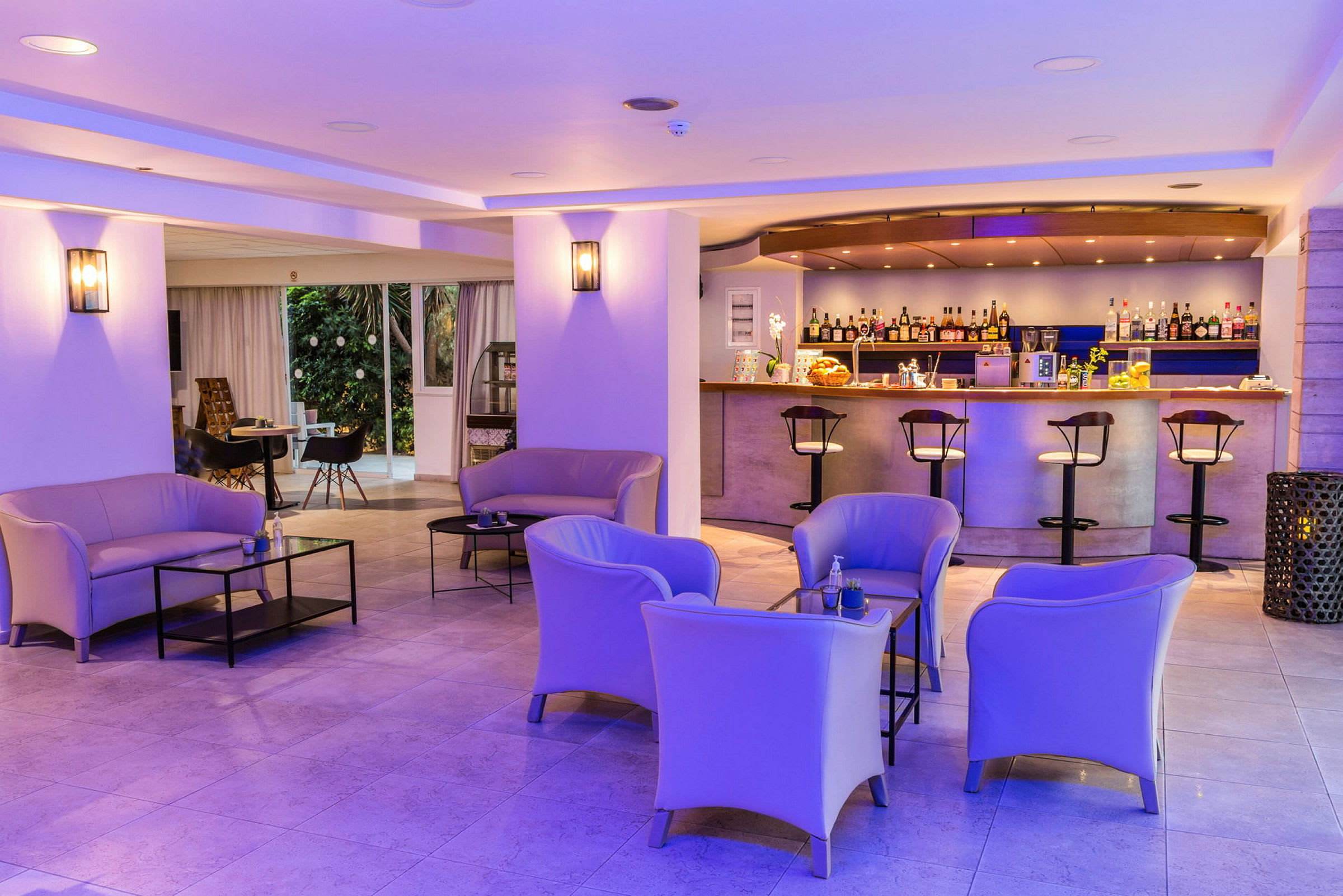 En hotellbar med sittgrupper och moderna möbler, belyst av lila takbelysning. (AI-genererad text)