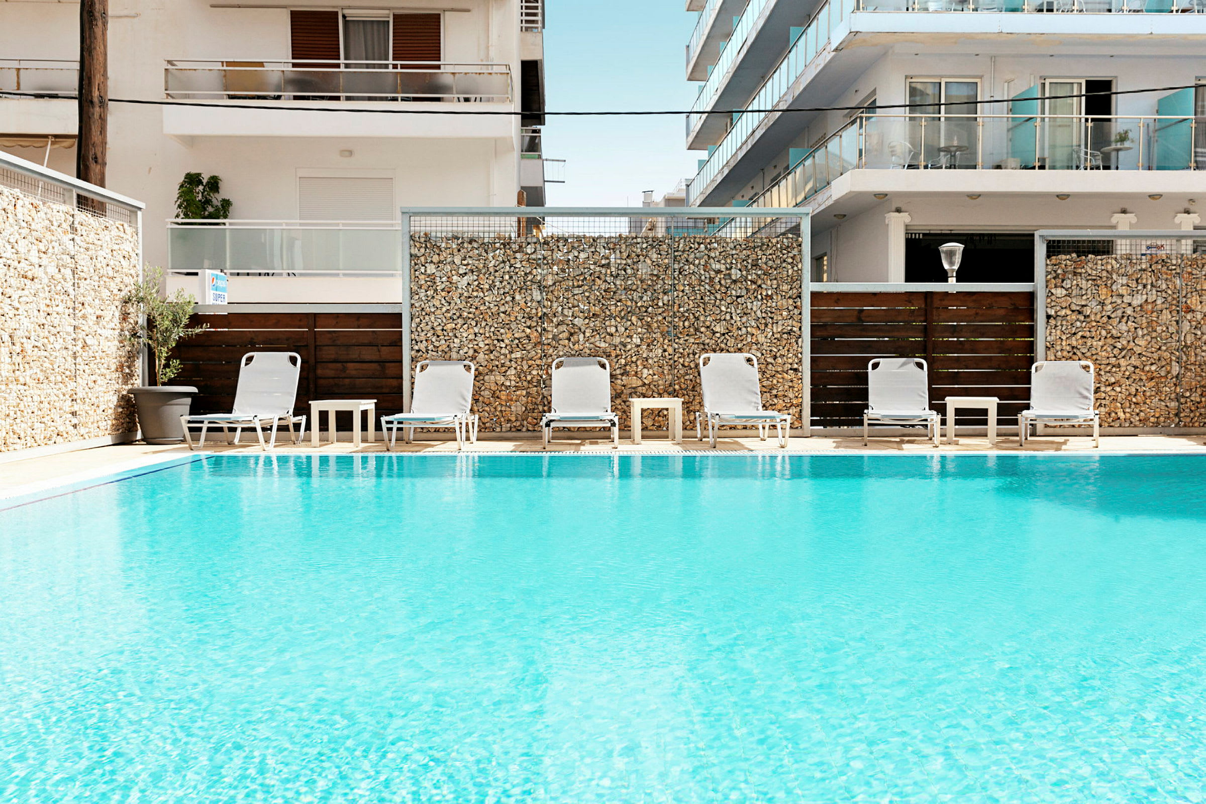 Pool med solstolar och bord framför byggnader. (AI-genererad text)