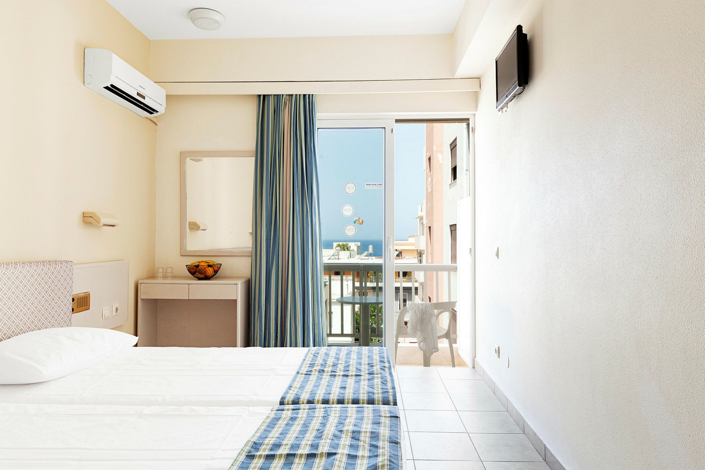 Hotellrum med två sängar, blågula sängöverkast, spegel, och en balkongdörr med utsikt. (AI-genererad text)