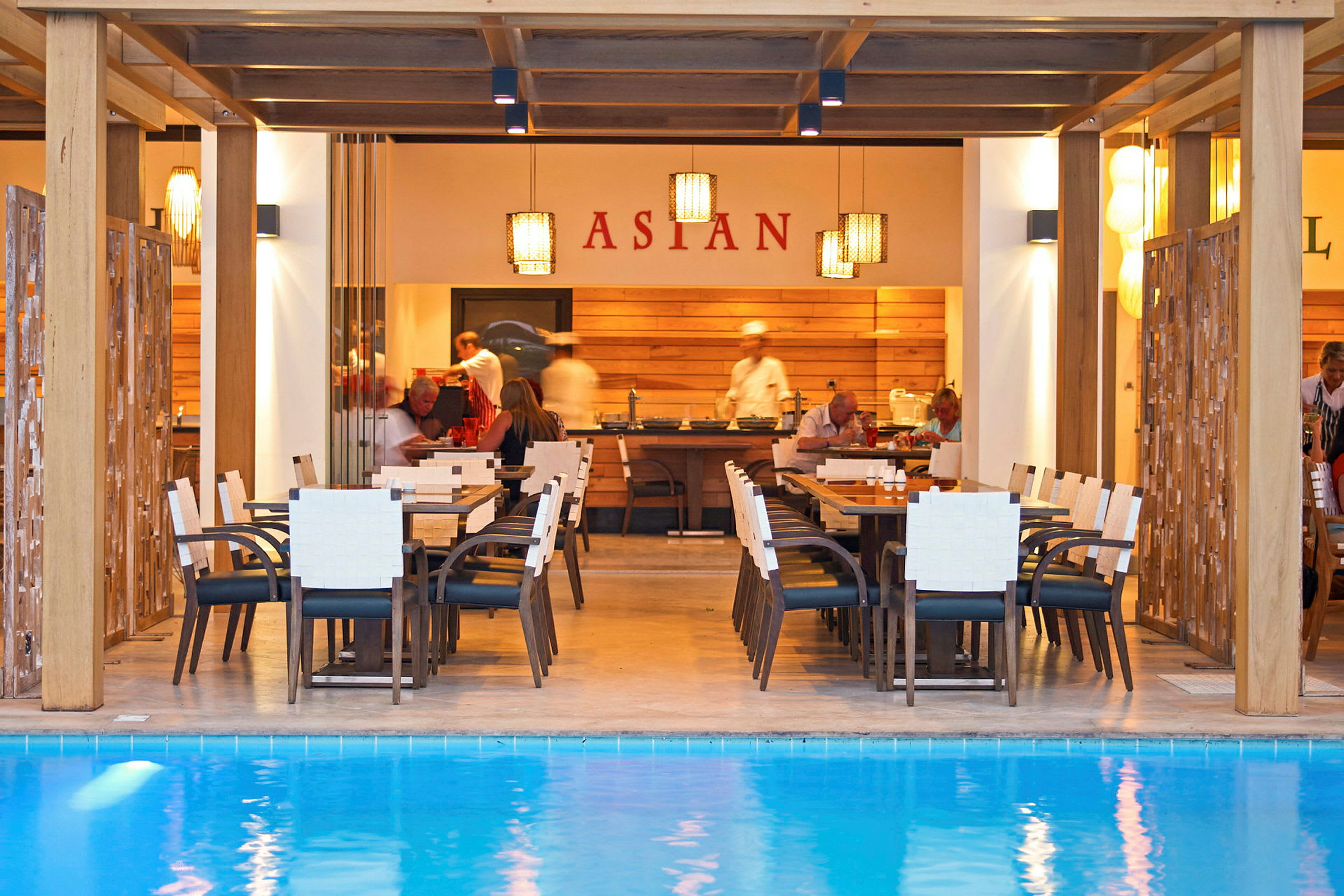 Restaurang vid en pool med bord och stolar framför en matservering. (AI-genererad text)