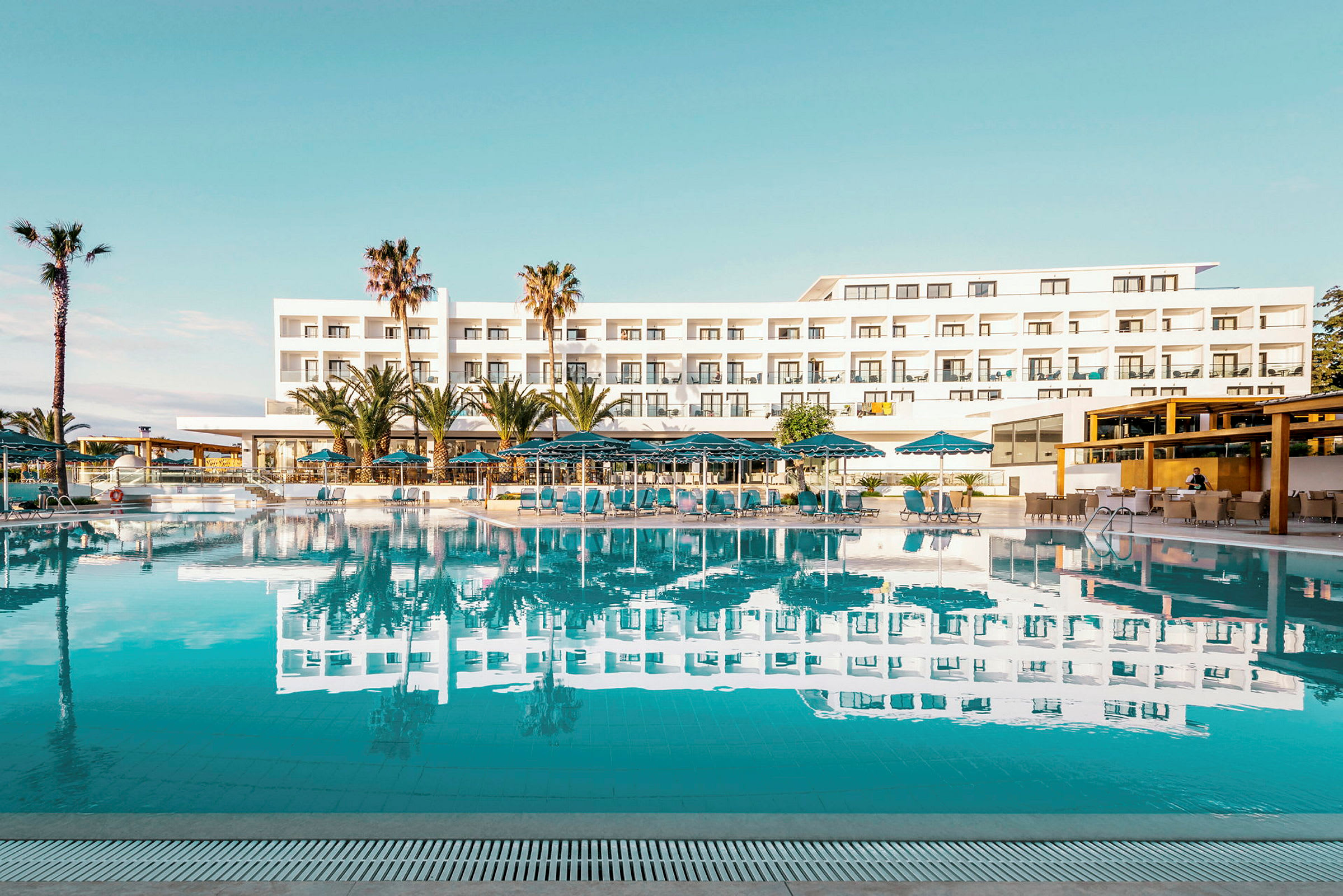 Hotellbyggnad med pool och solstolar i förgrunden. (AI-genererad text)