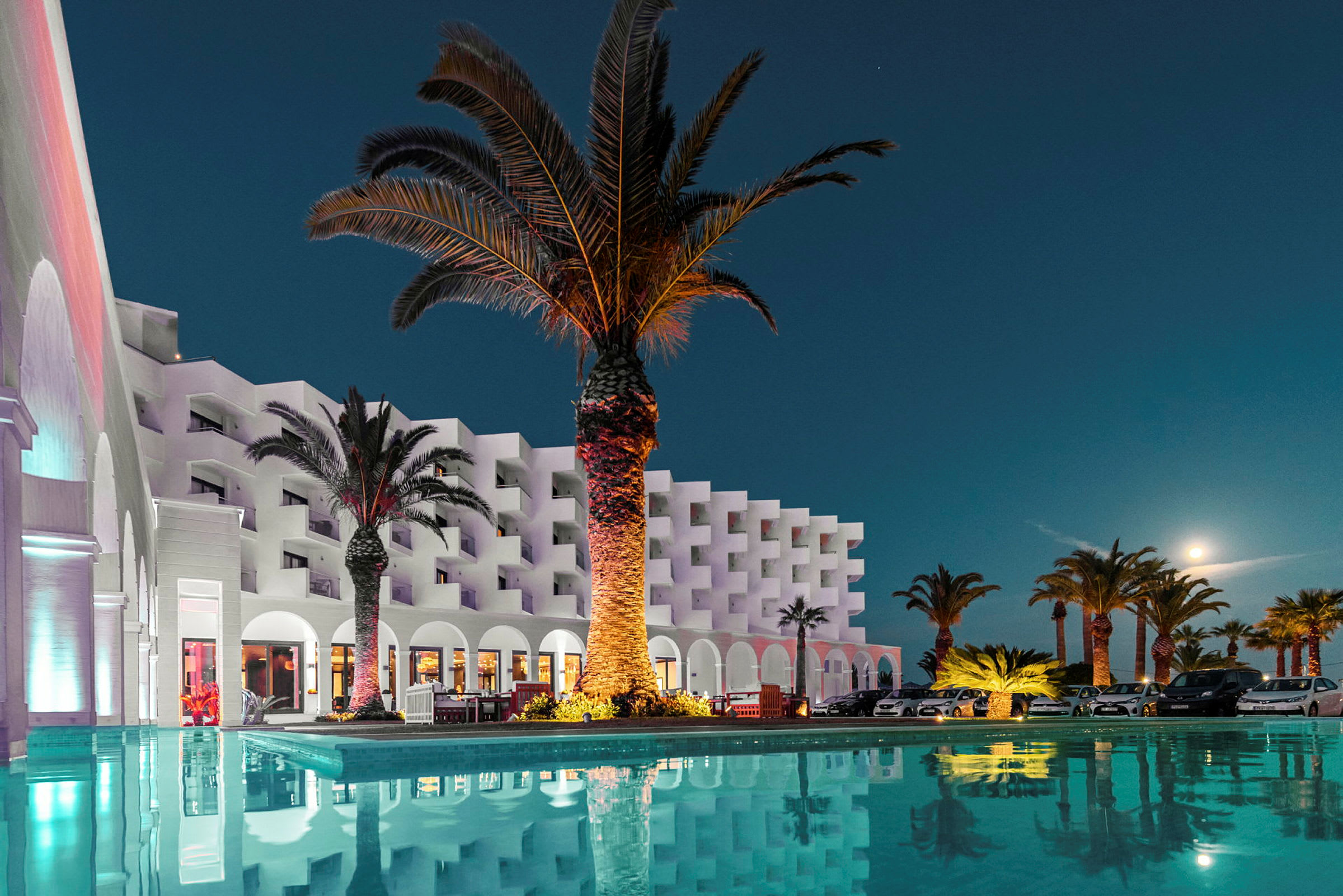 Ett semesterhotell med palmer och pool under en klar natthimmel. (AI-genererad text)