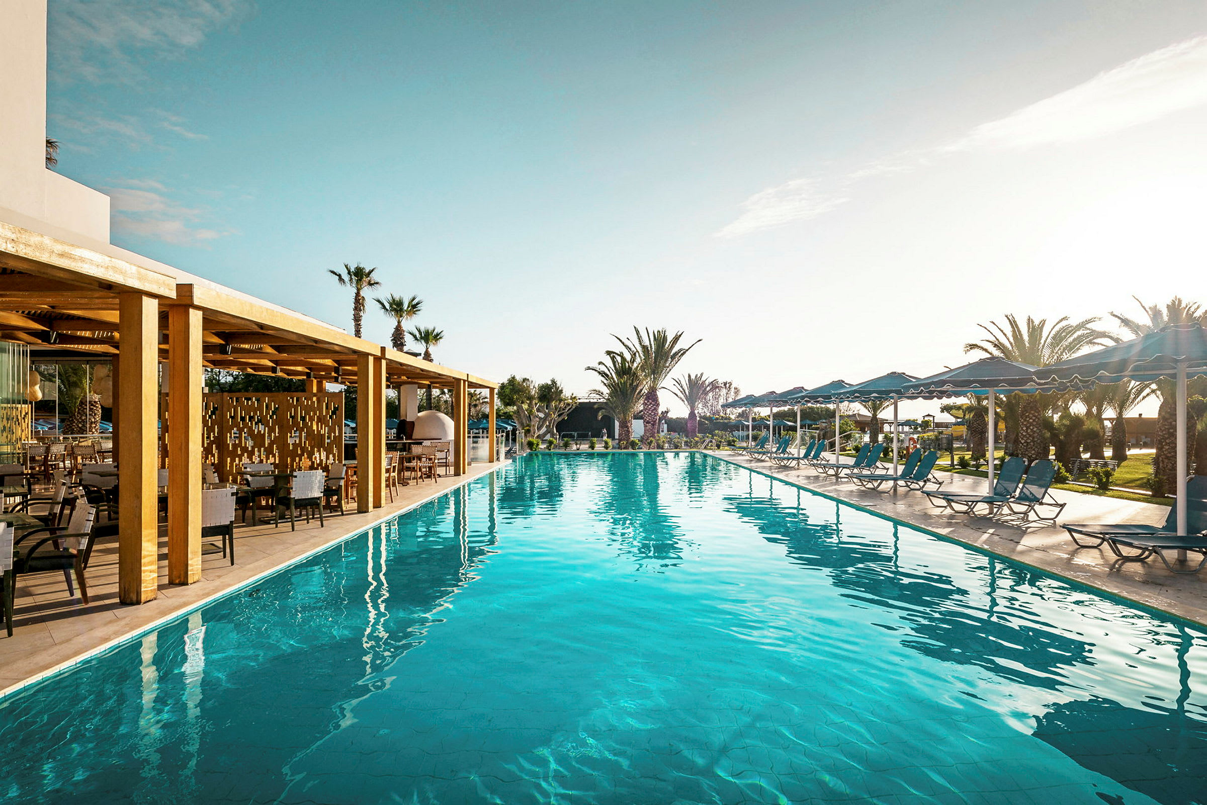 En pool med solstolar och parasoller, samt en träbeklädd terrass bredvid. (AI-genererad text)