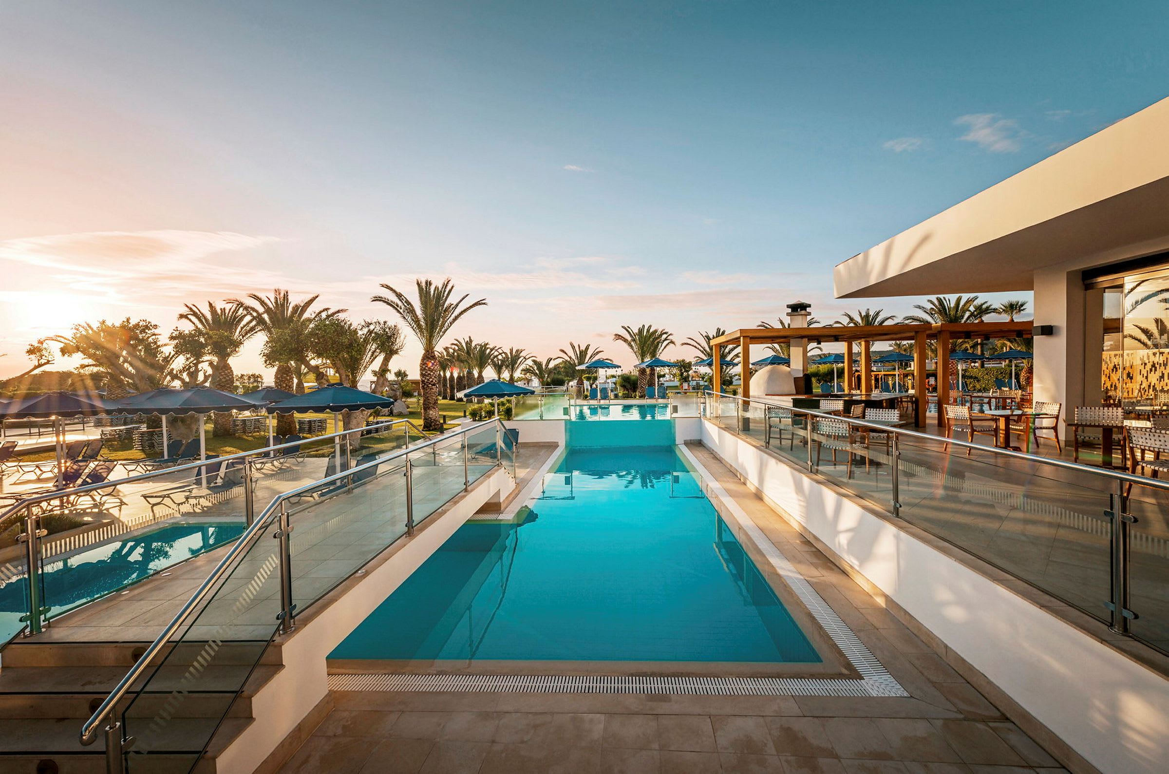 En swimmingpool vid ett hotell, omgiven av palmer och solstolar under ett klart himmel. (AI-genererad text)