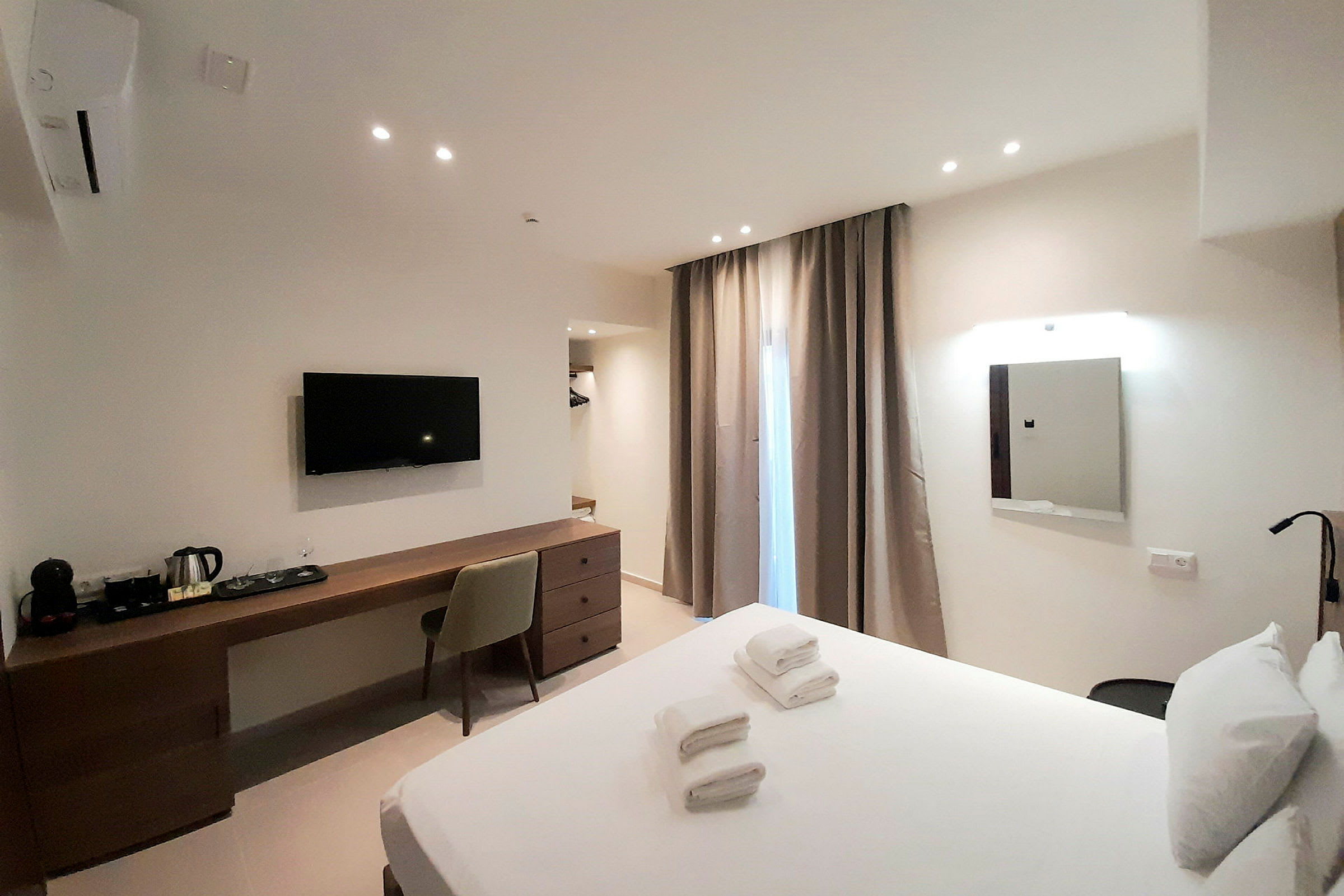 Ett hotellrum med en bäddad säng, skrivbord med stol, väggmonterad TV och gardiner vid ett fönster. (AI-genererad text)