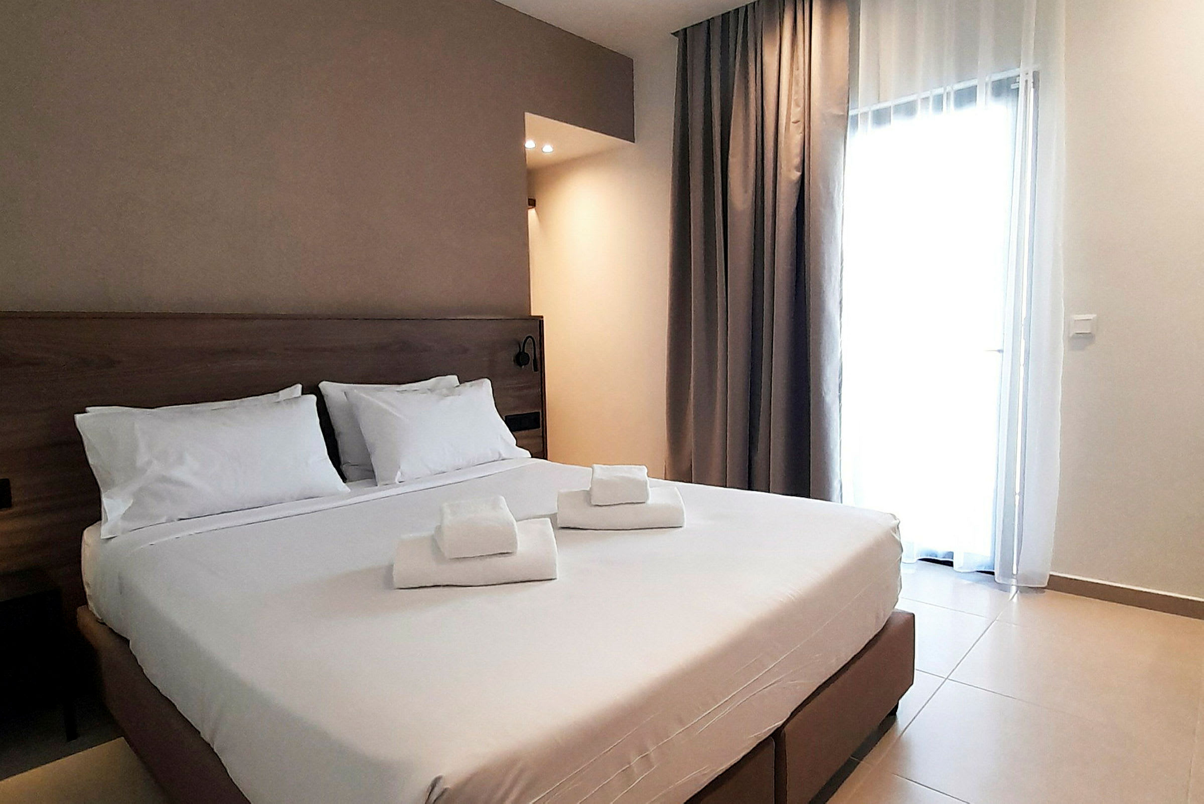 Ett hotellrum med en dubbelsäng och vita lakan, samt vikta handdukar placerade på sängen. (AI-genererad text)