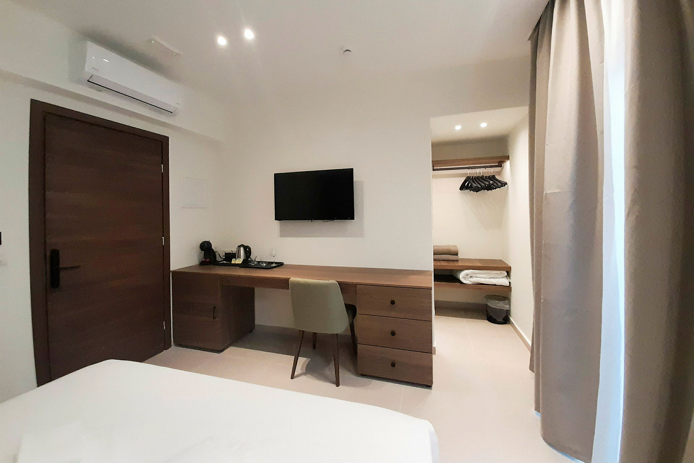 Hotellrum med skrivbord, stol, TV, garderob och luftkonditionering. (AI-genererad text)