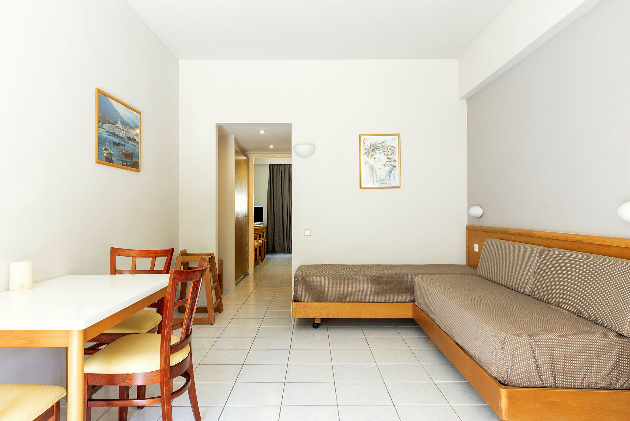 Bild av ett hotellrum med ett bord, stolar, en soffa och en vy mot en korridor. (AI-genererad text)