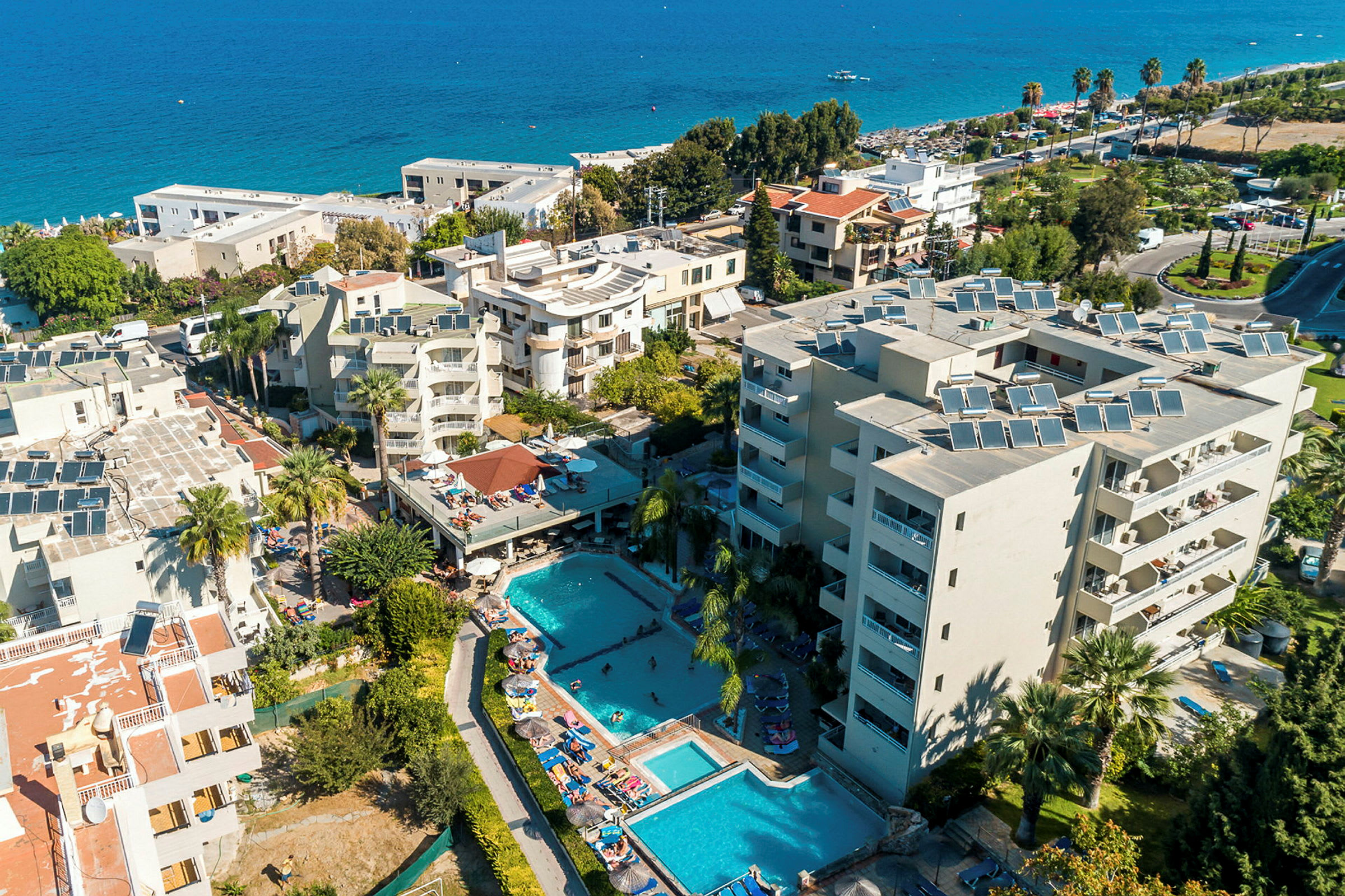 Flygfoto av hotellområde med byggnader, pooler och omgivande grönska vid havet. (AI-genererad text)