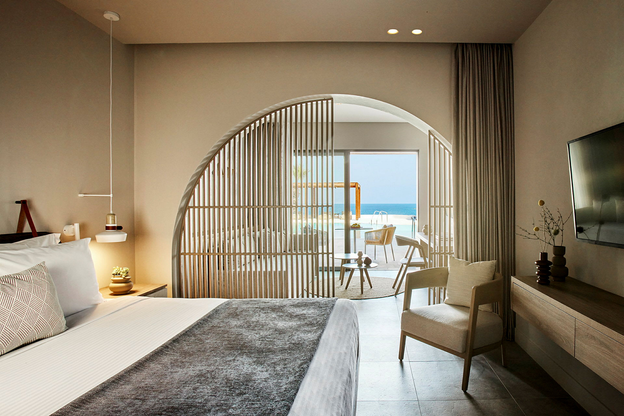 Interiör av ett hotellrum med säng, sittmöbler och utsikt över pool och hav. (AI-genererad text)