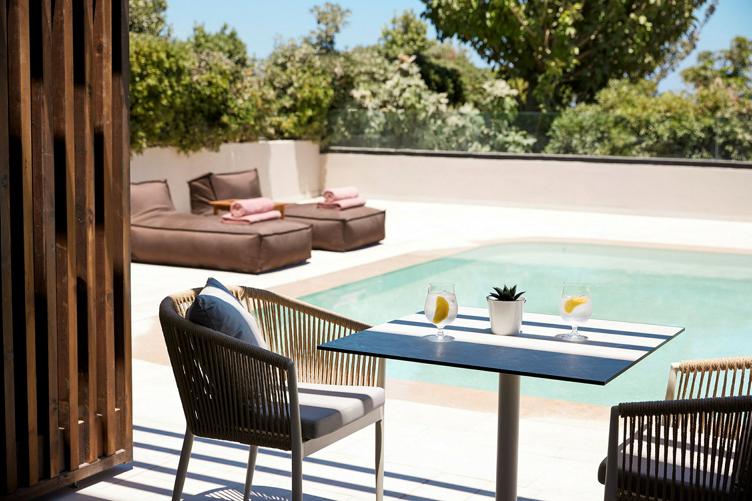 Ett bord med två glas vatten och en liten växt vid en pool, med solstolar i bakgrunden. (AI-genererad text)