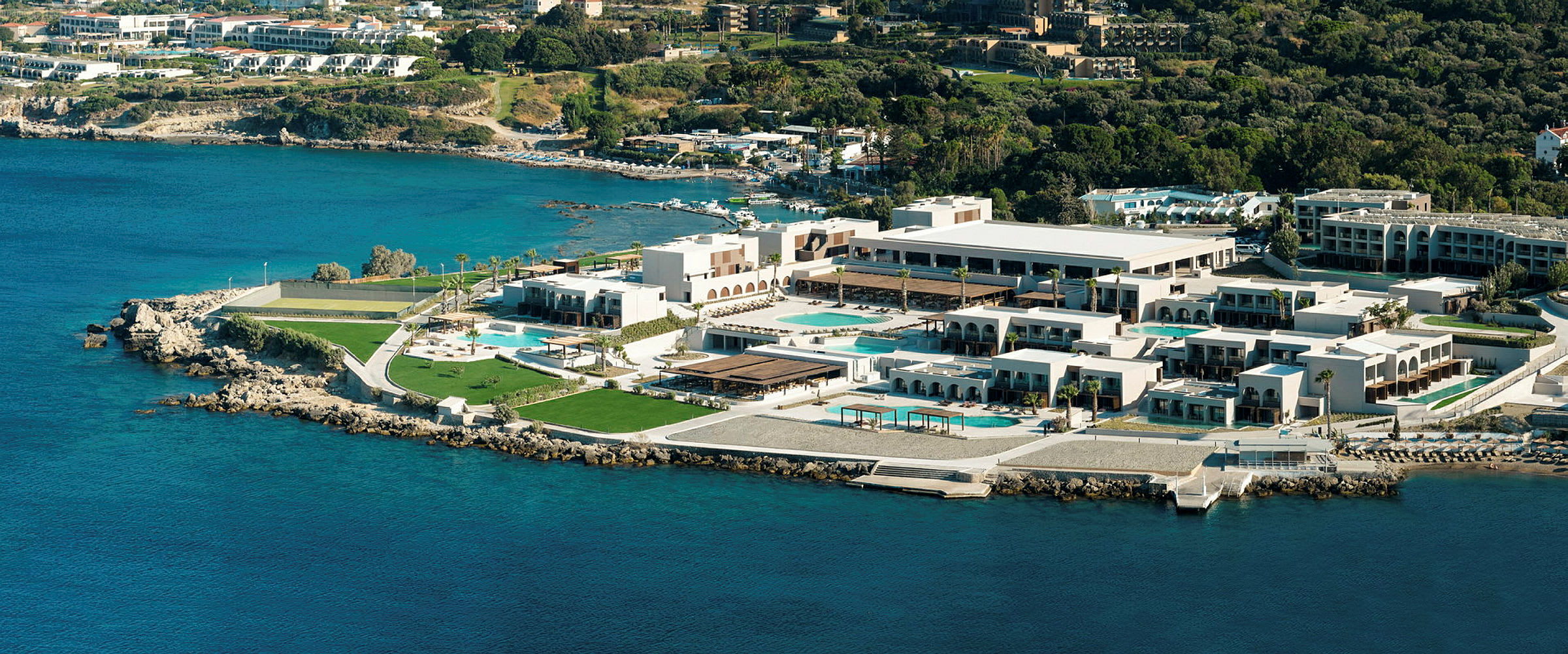 Flygvy över ett hotellkomplex vid kusten, med pooler och grönområden. (AI-genererad text)