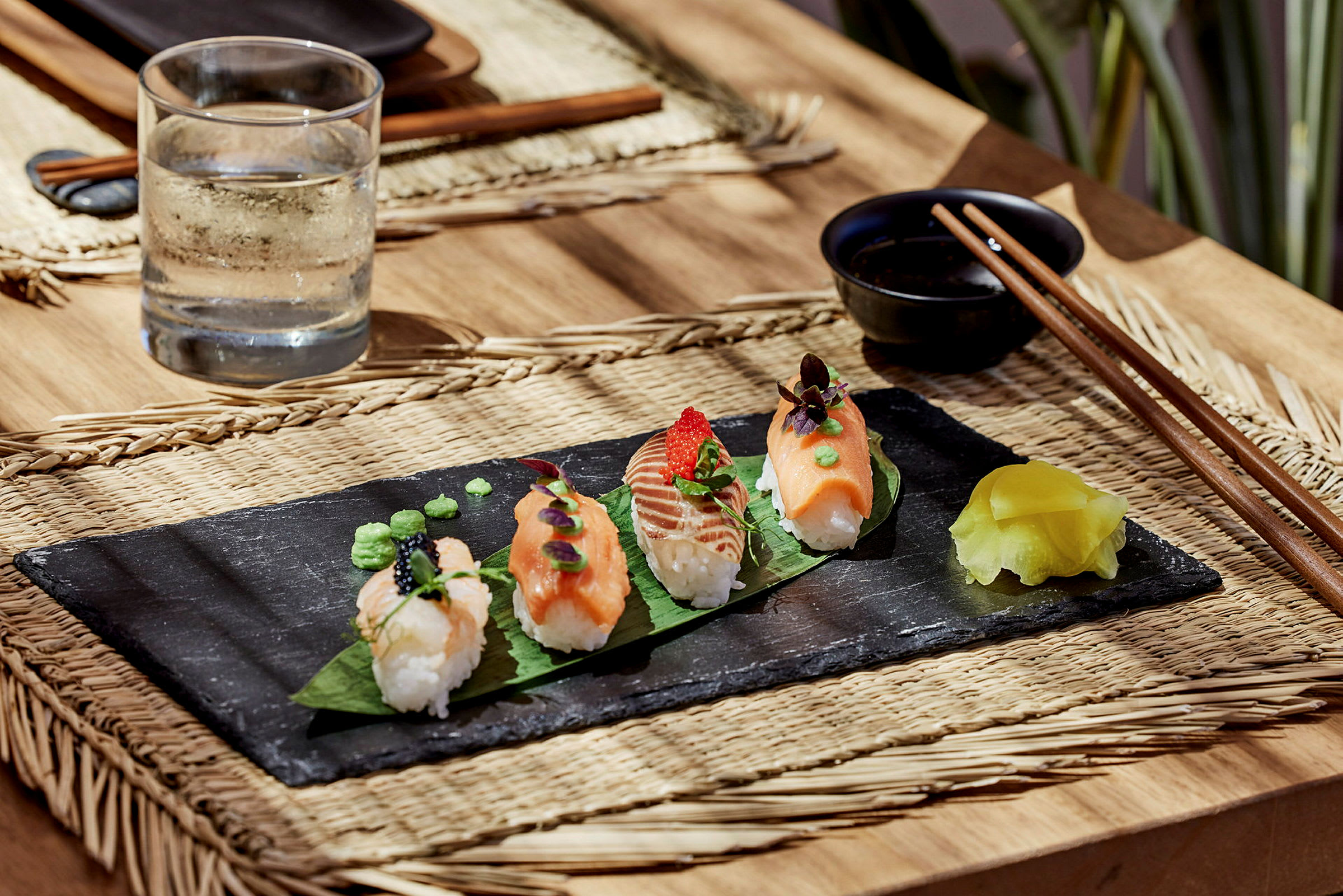 Sushibitar på ett svart fat med en kanna vatten och ätpinnar bredvid. (AI-genererad text)