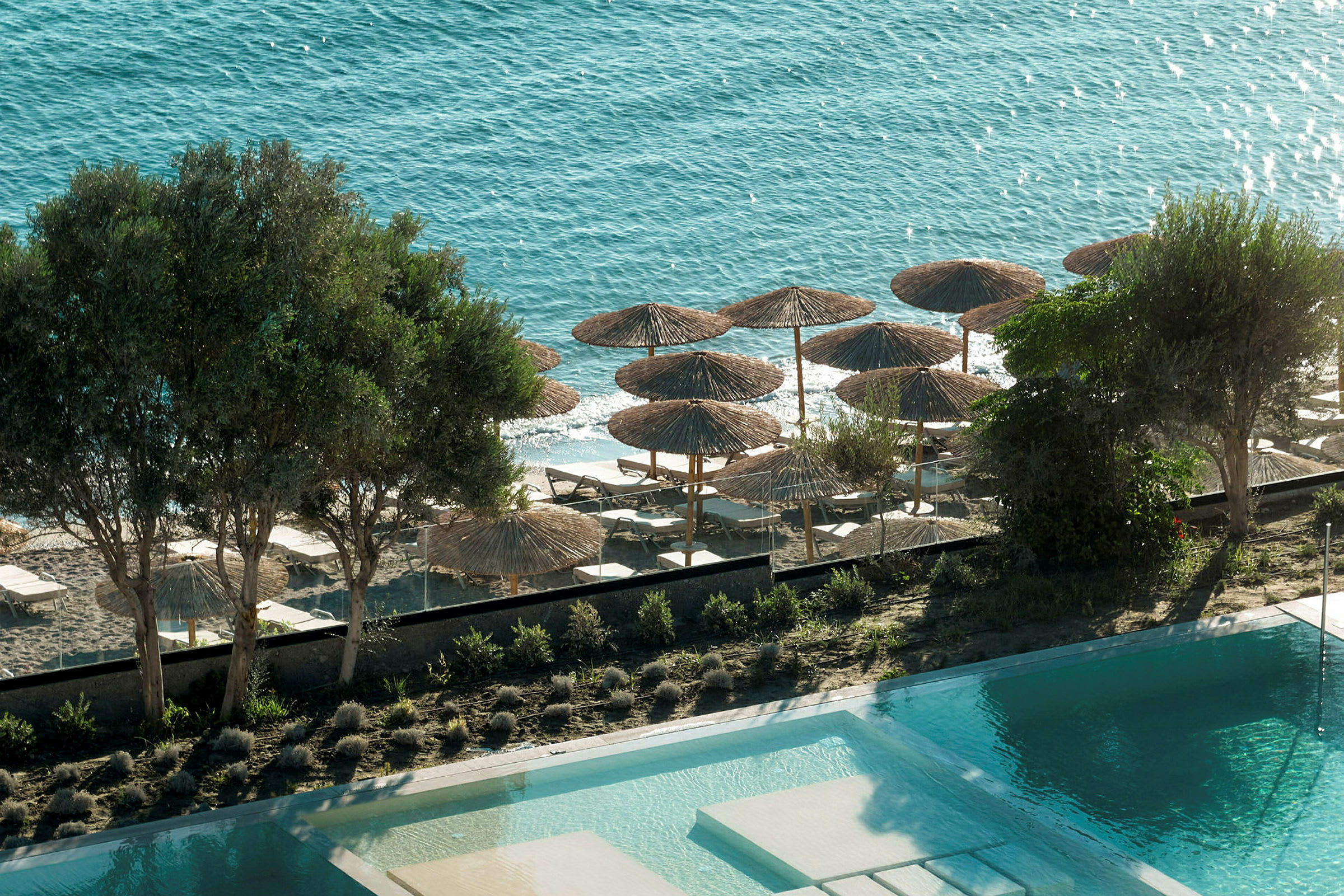 Pool med en sandstrand och parasoller vid havet. (AI-genererad text)