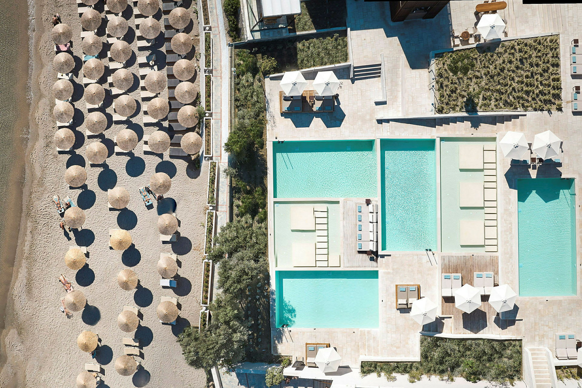 Flygfoto som visar en strand med parasoller och solstolar samt poolområden med solstolar och parasoller. (AI-genererad text)