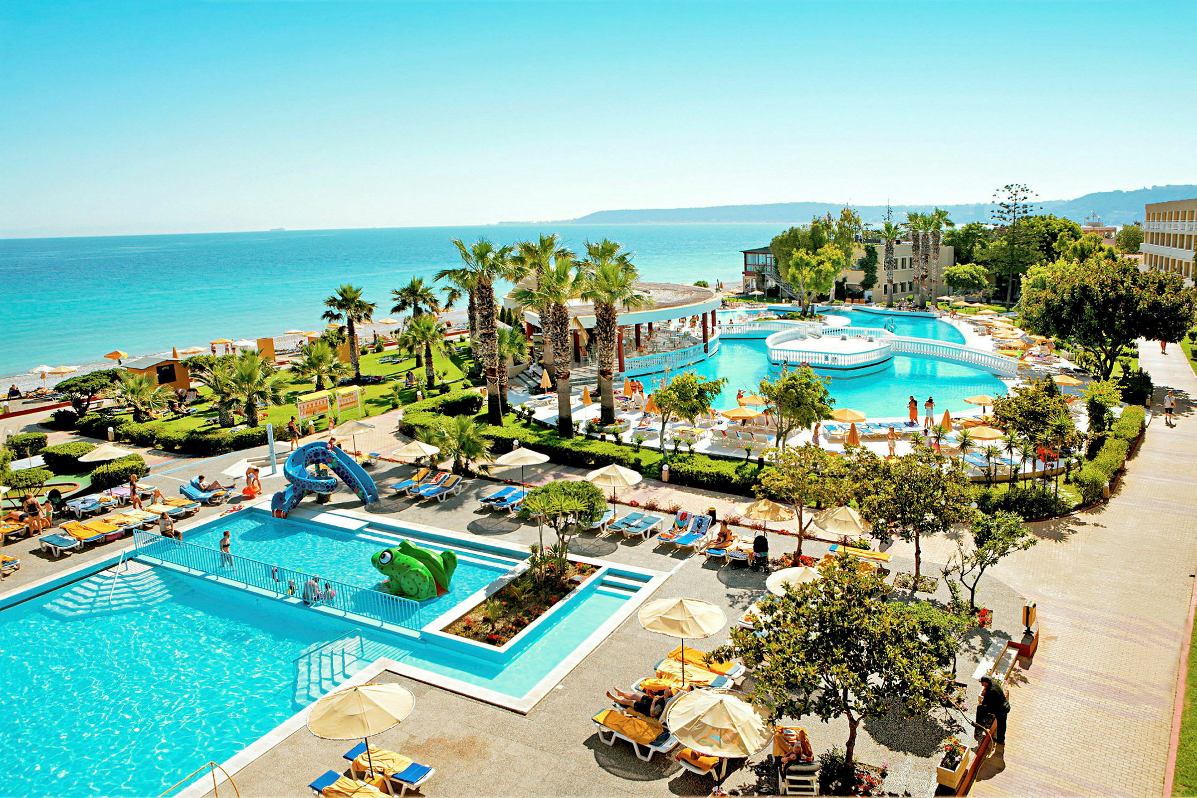 En hotellresort med poolområde och grönskande trädgård vid en strand med havsutsikt. (AI-genererad text)
