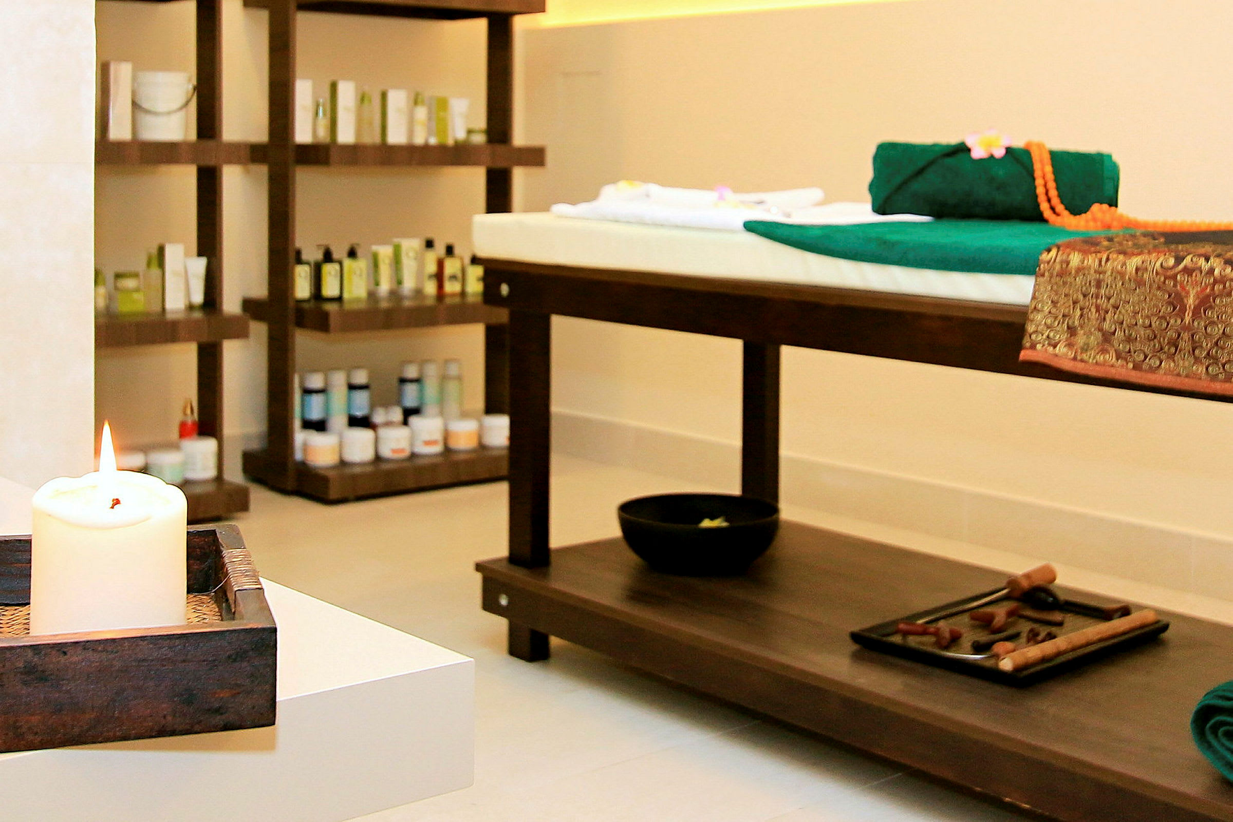 Ett spa-rum med massagebrits och hyllor fyllda med produkter, samt en tänd ljus i förgrunden. (AI-genererad text)