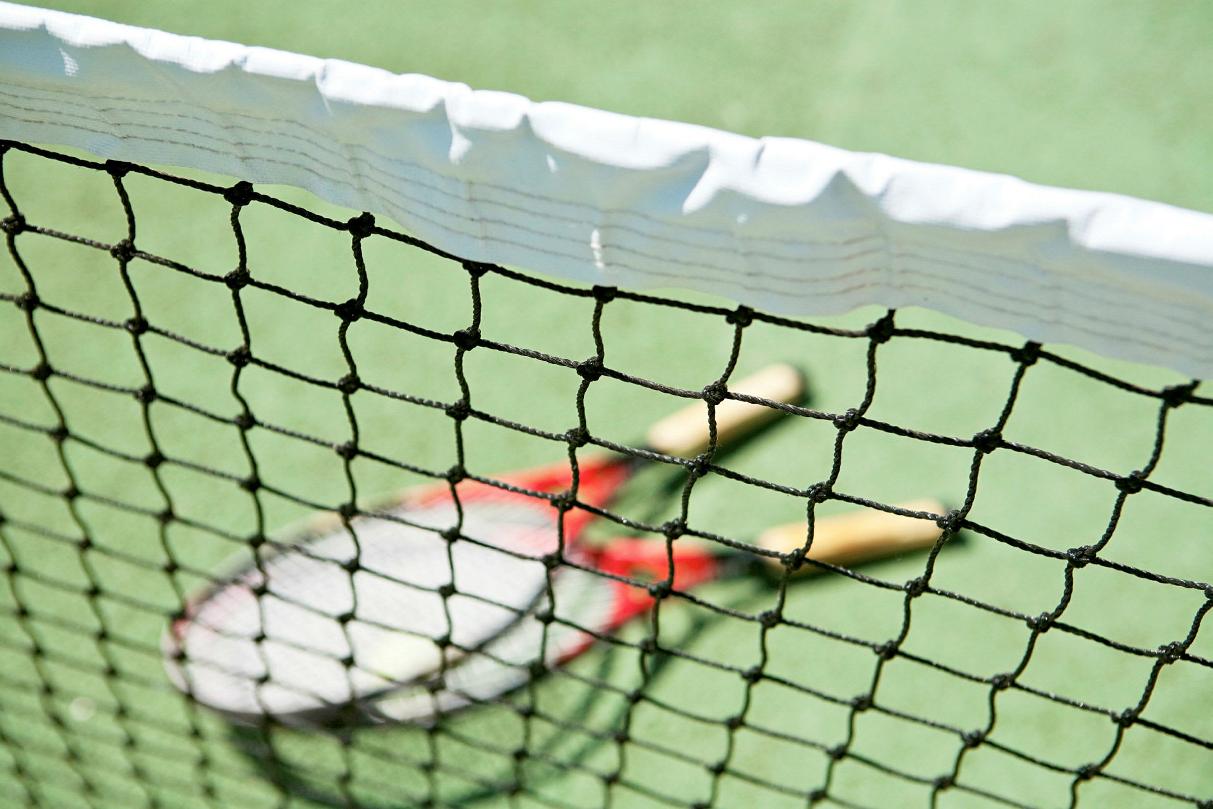 Närbild av ett tennisnät med två tennisracketar på planen bakom. (AI-genererad text)