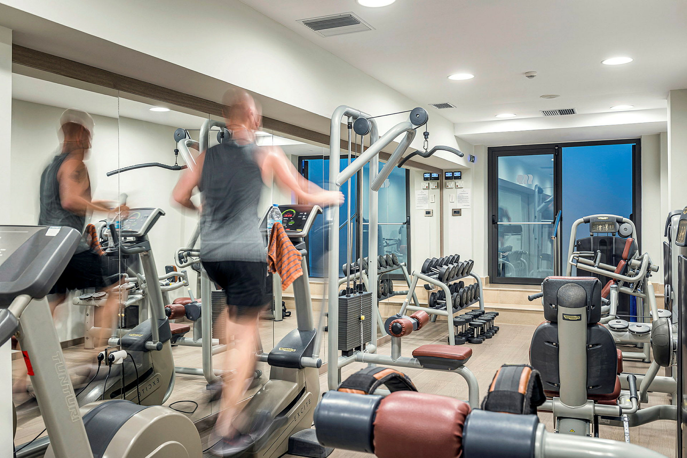 Ett gym med olika träningsmaskiner och hantlar, samt en person som tränar på en löpmaskin. (AI-genererad text)