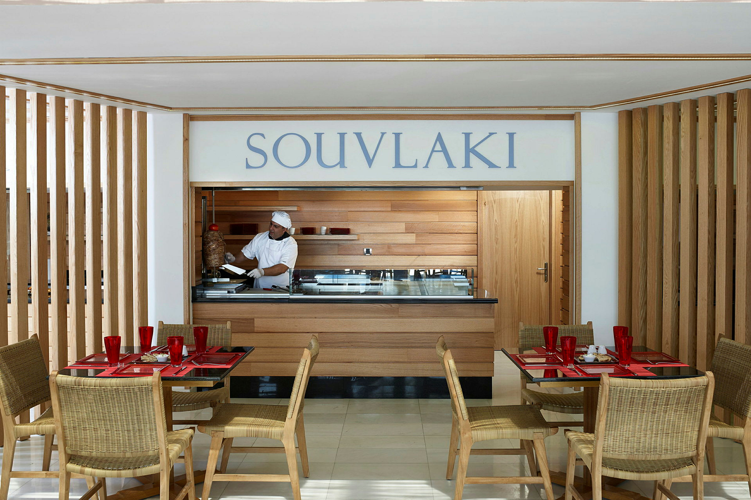En restaurang med en souvlaki-servering. Bord och stolar är placerade i förgrunden. (AI-genererad text)