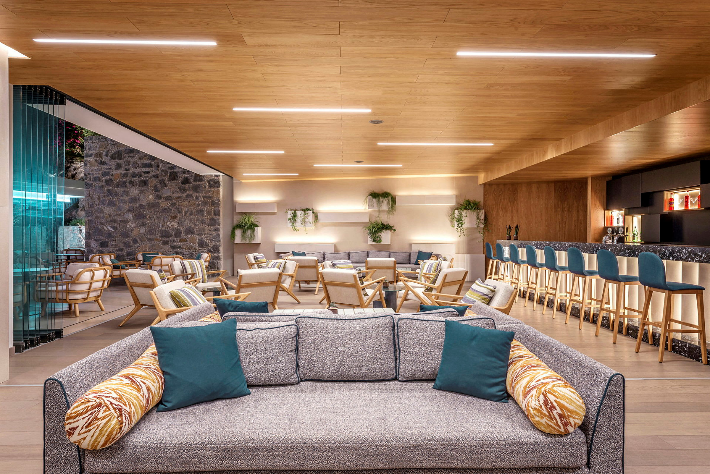 Ett modernt och inbjudande loungeområde med soffor, fåtöljer och en bar med sittplatser. Inredningen är ljus och luftigt med trädetaljer och grönska. (AI-genererad text)