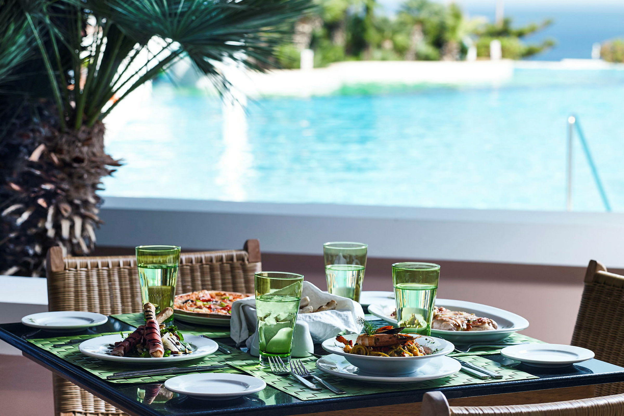 Ett dukat bord med maträtter och glas, med utsikt över en pool och omgivande grönska. (AI-genererad text)