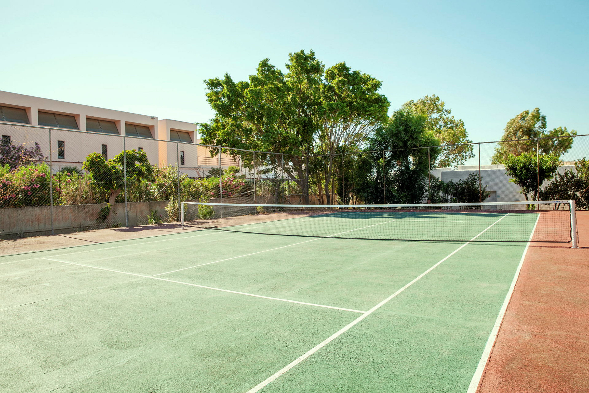 En tennisbana med grön yta och nät, omgiven av träd och byggnader. (AI-genererad text)