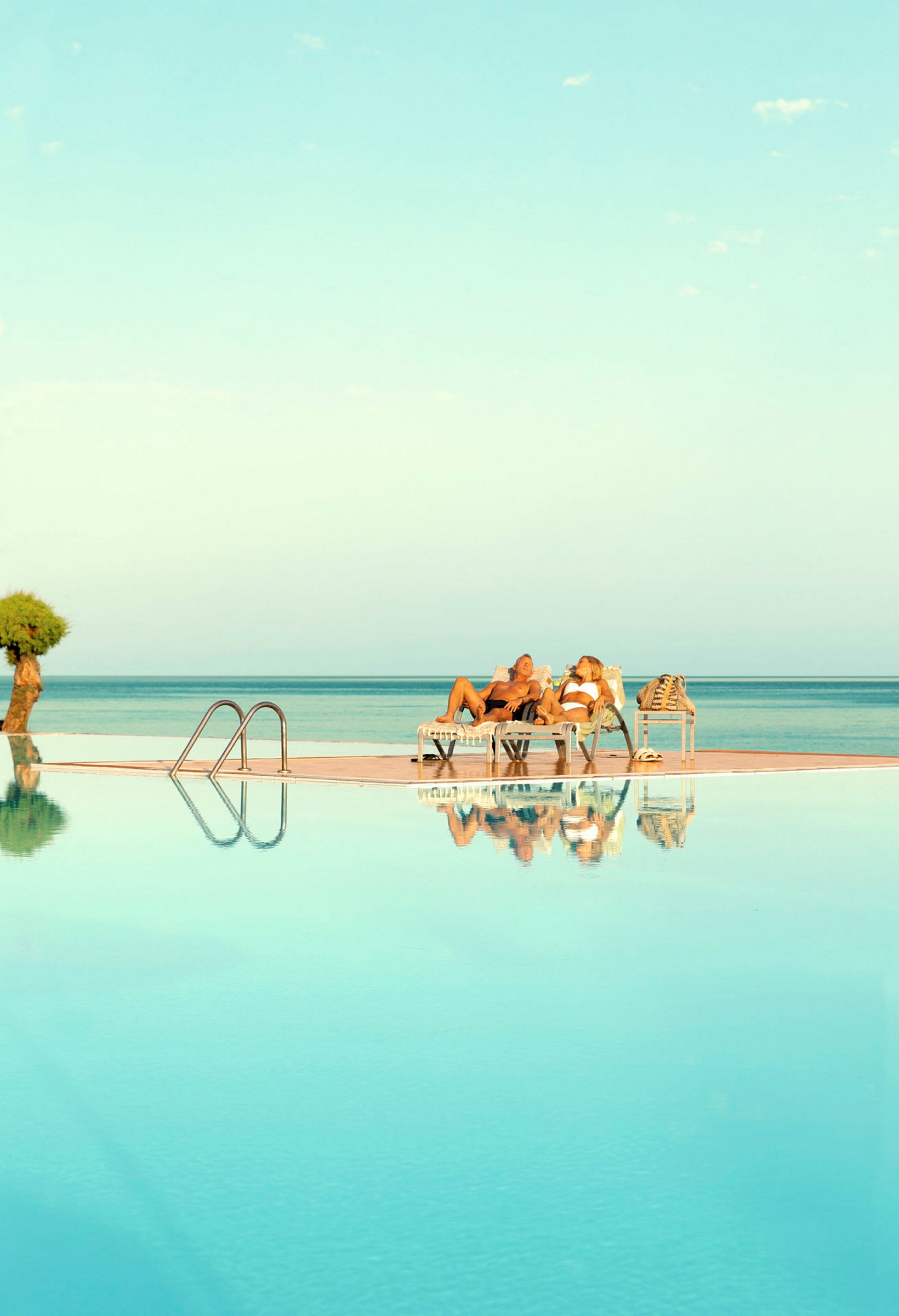 Personer som ligger på solstolar vid en pool med utsikt mot havet. (AI-genererad text)
