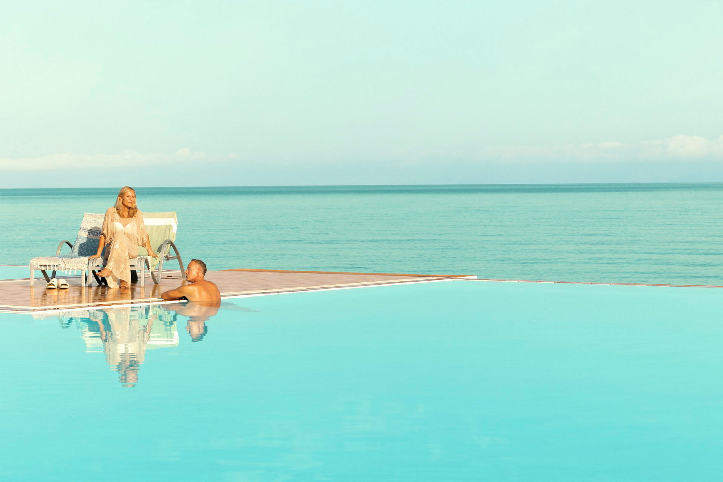En infinitypool med utsikt över havet, med en person vid poolkanten och en annan på en solstol. (AI-genererad text)