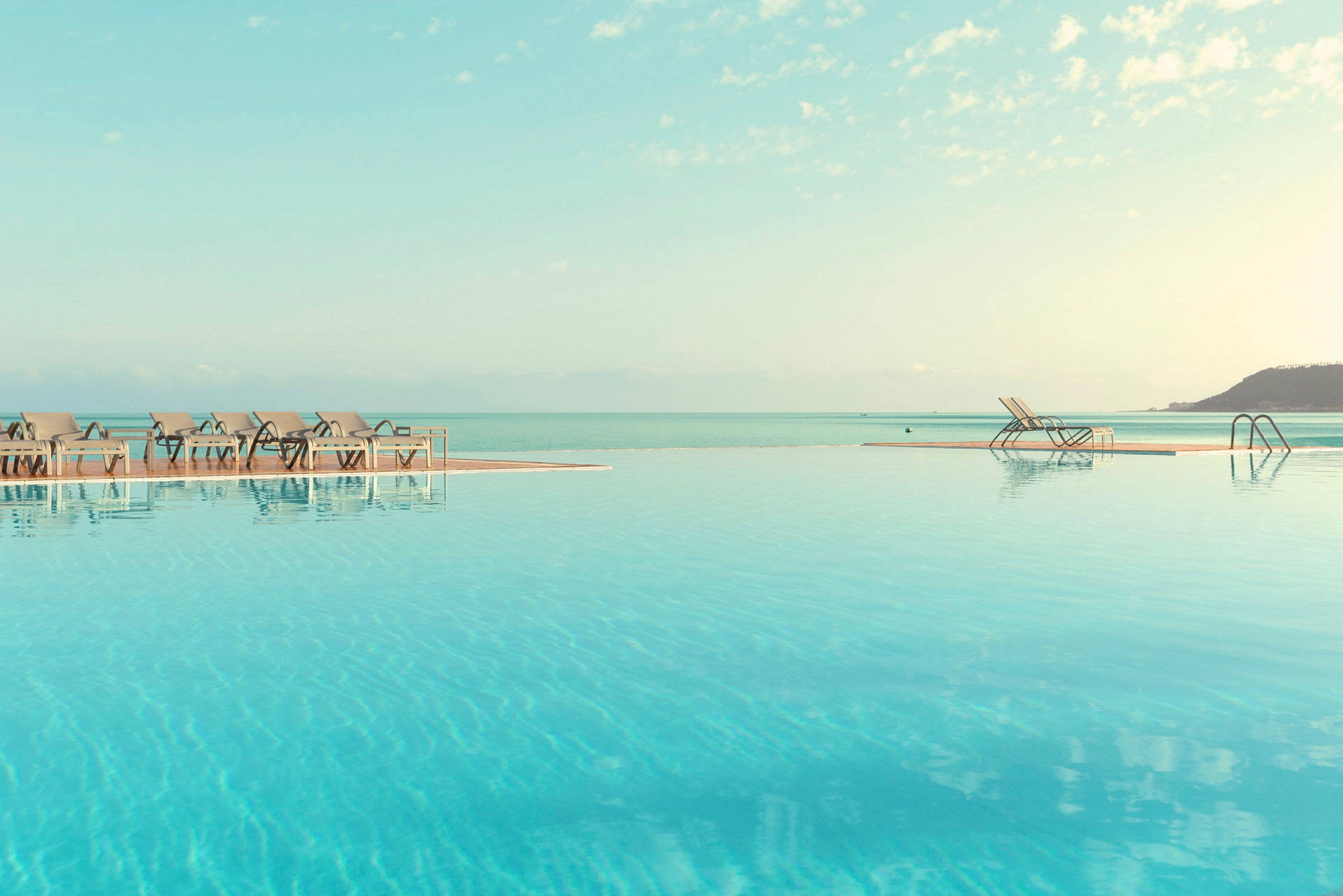 En infinitypool med utsikt över havet, samt solstolar vid kanten. (AI-genererad text)