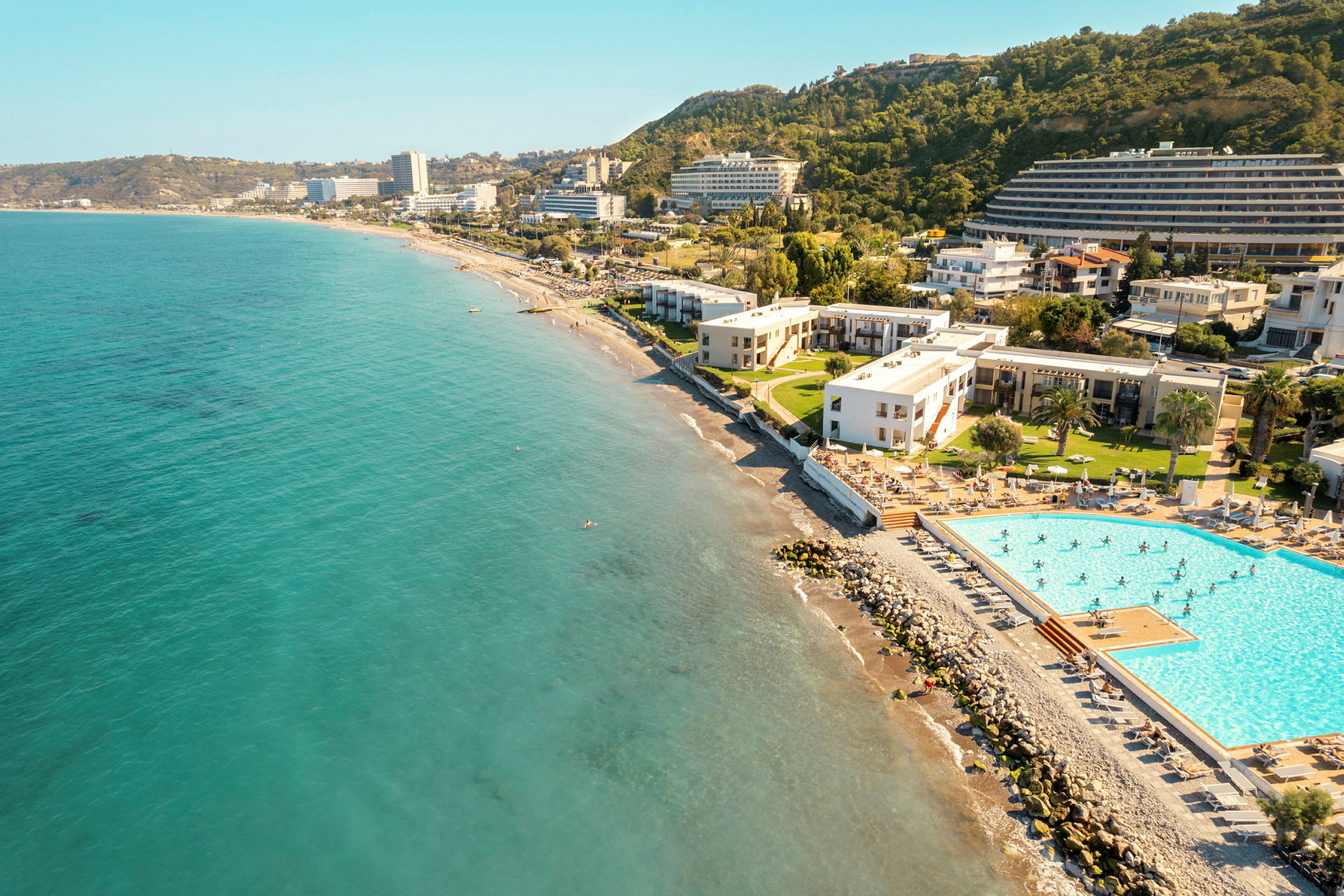 Flygfoto av en kust med havet, hotellbyggnader och en pool. (AI-genererad text)