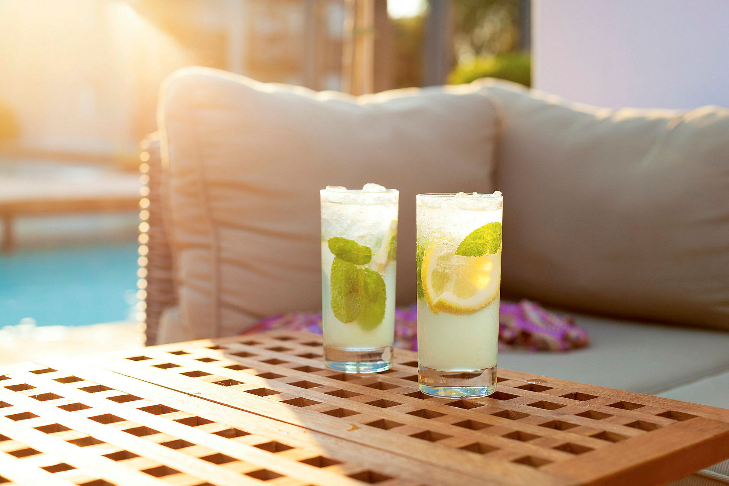 Två svalkande drinkar med citron och mynta på ett träbord nära en pool. (AI-genererad text)