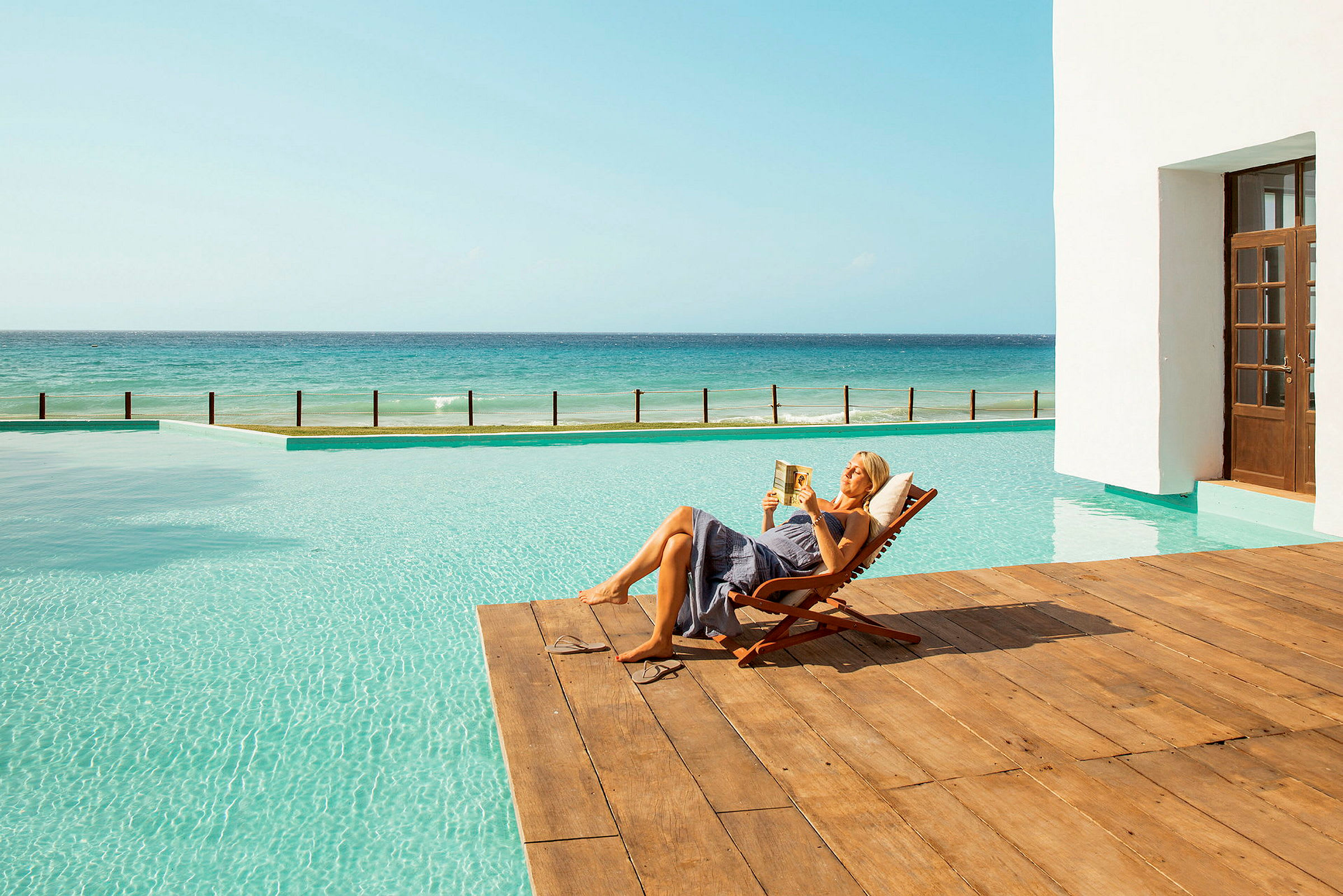 Person ligger på en solstol vid en pool nära havet. (AI-genererad text)