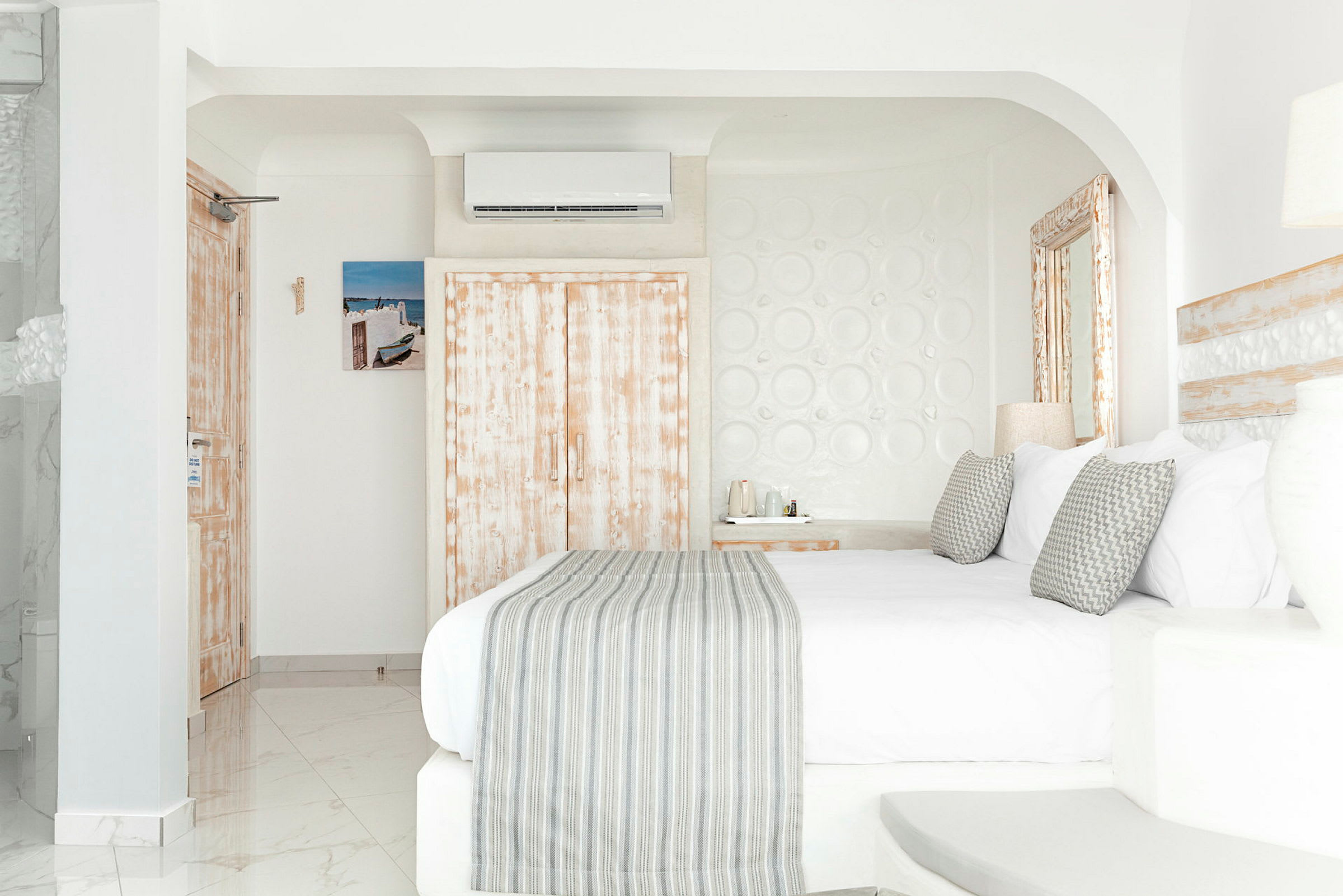 Ett hotellrum med ljus inredning, säng med dekorativa kuddar och väggar i neutral färg. (AI-genererad text)