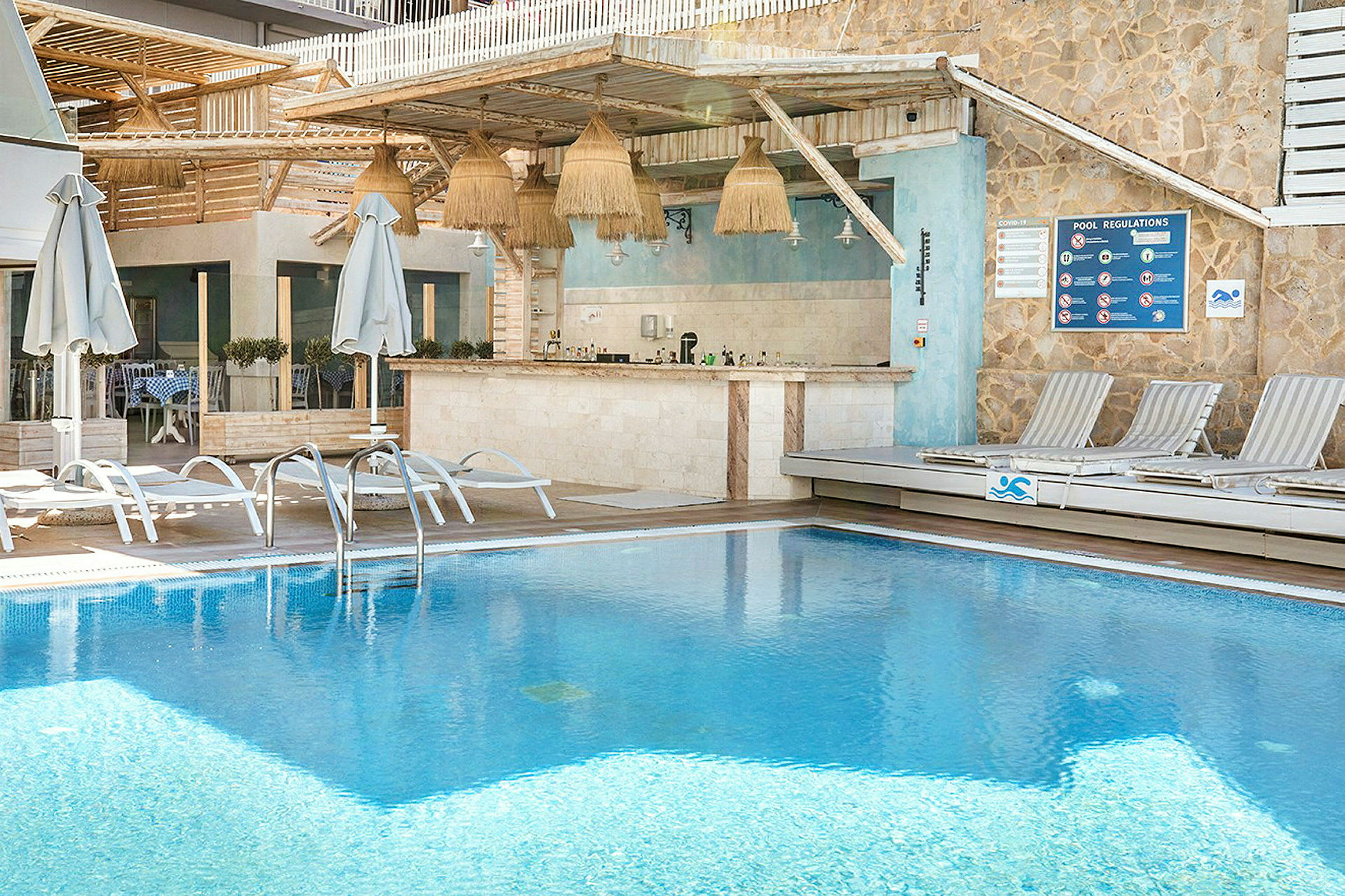 Utomhuspool med solstolar och en bar i bakgrunden. (AI-genererad text)