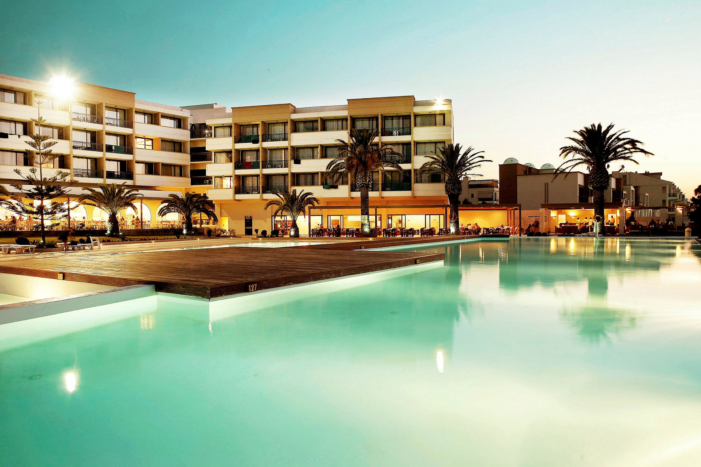 Hotellbyggnad med palmer i gryningen, framför en pool. (AI-genererad text)