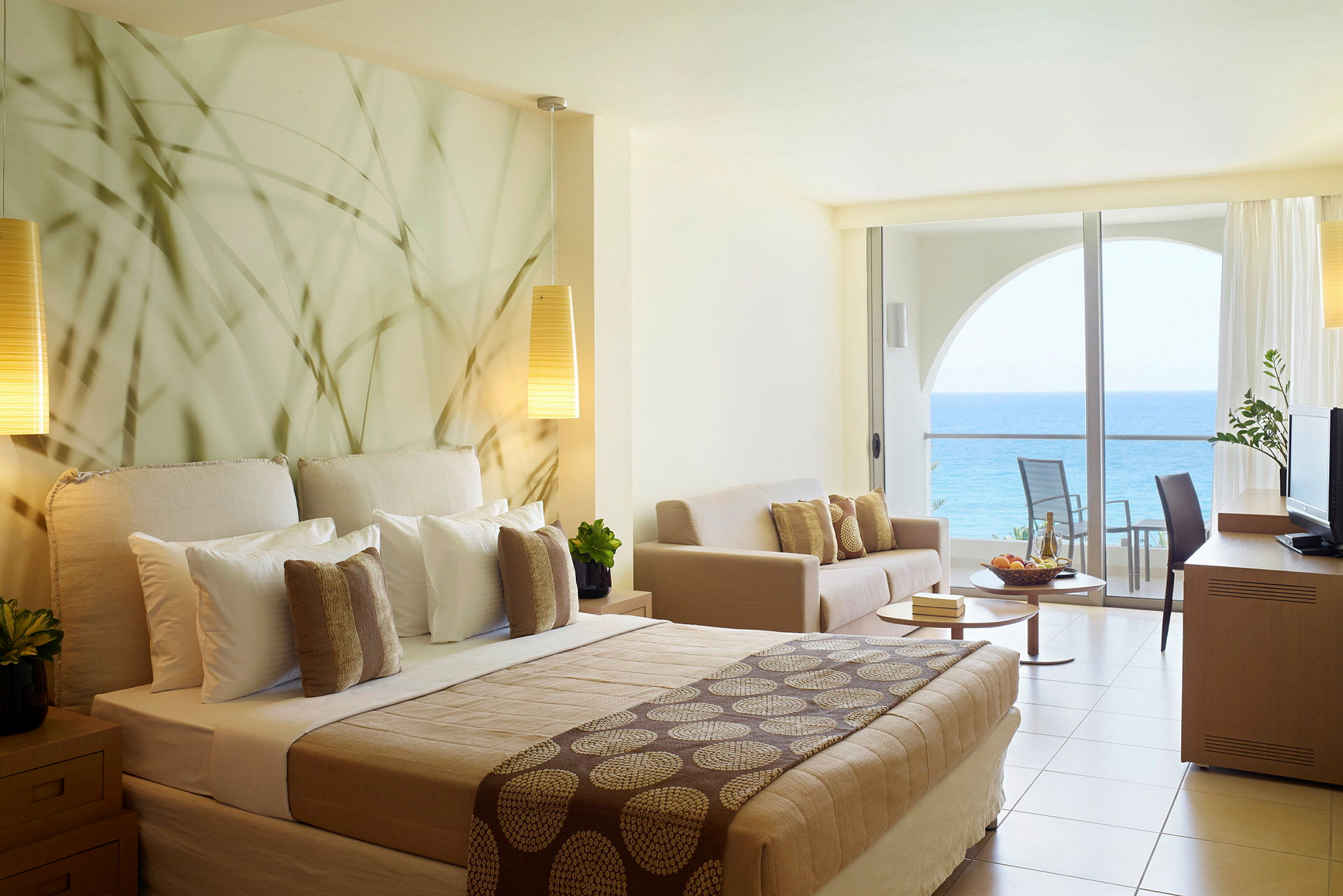 Hotellrum med havsutsikt och modern inredning inklusive säng, soffa och balkong. (AI-genererad text)
