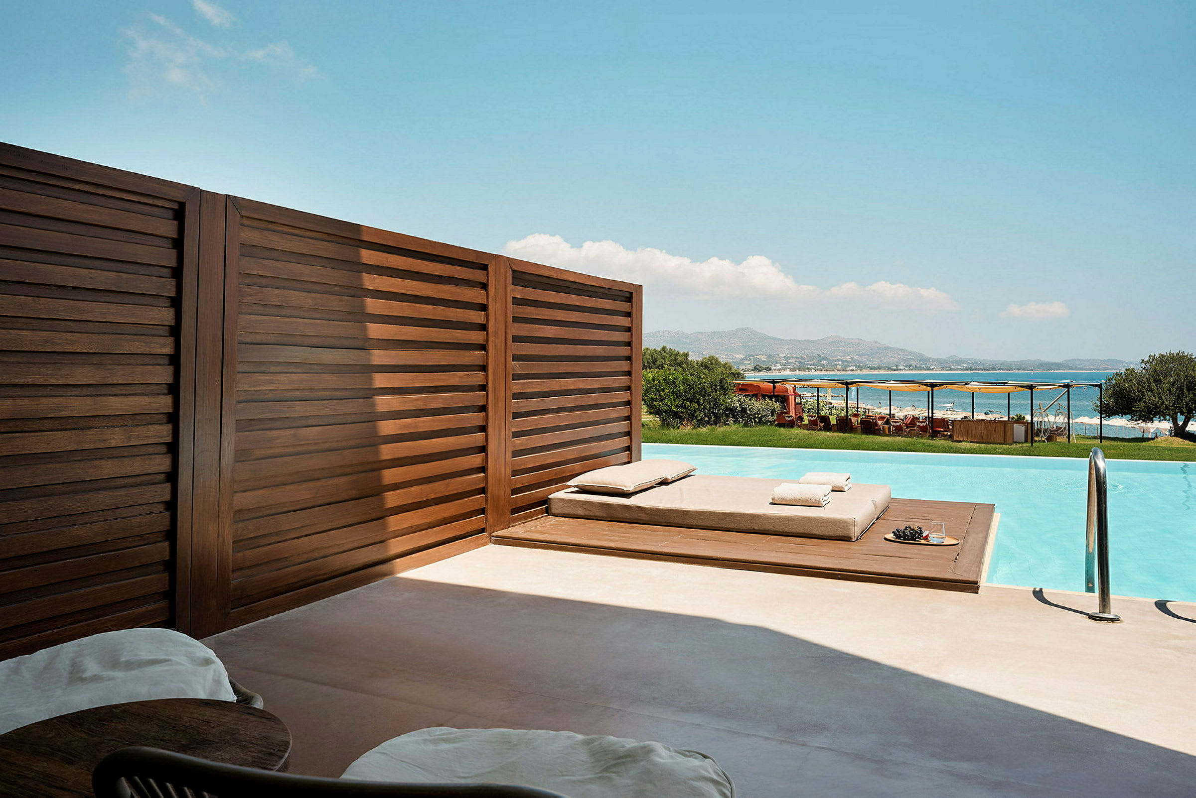 Privat poolområde med solstolar, träpanel och utsikt över havet. (AI-genererad text)
