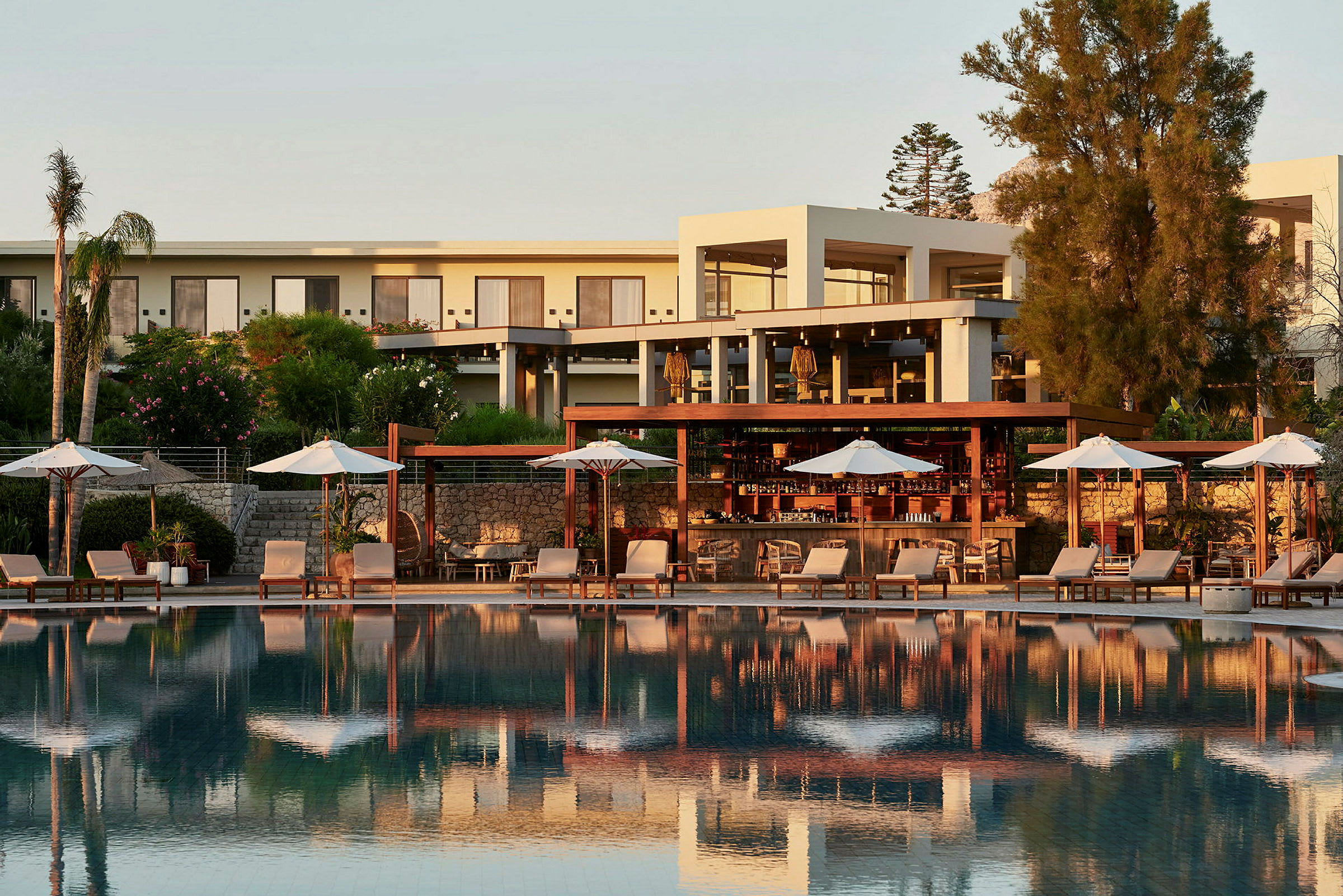Poolområde med solstolar och parasoller framför en hotellbyggnad. (AI-genererad text)