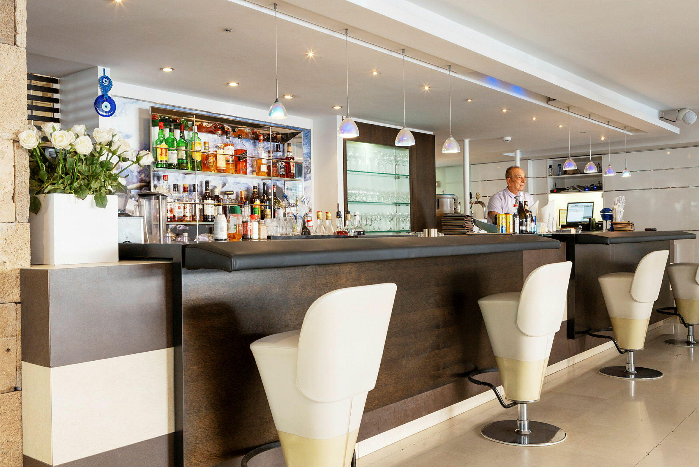 En hotellbar med elegant inredning inklusive en sittdel med höga stolar och flaskor samt glas på en hylla. (AI-genererad text)