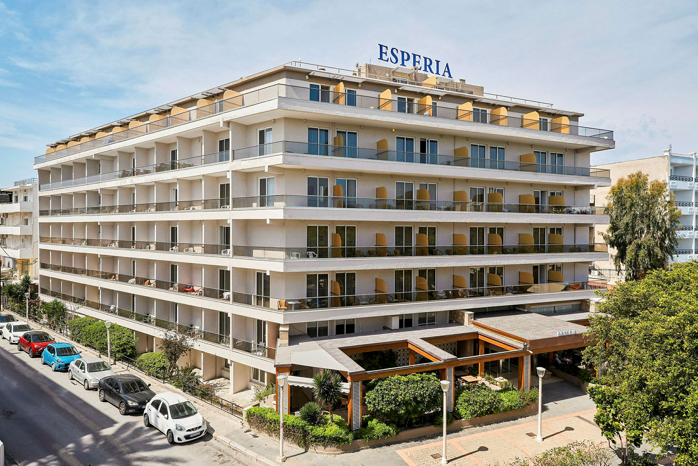 Hotel Esperia, ett flervåningshus med stora balkonger och gröna planteringar vid entrén. (AI-genererad text)
