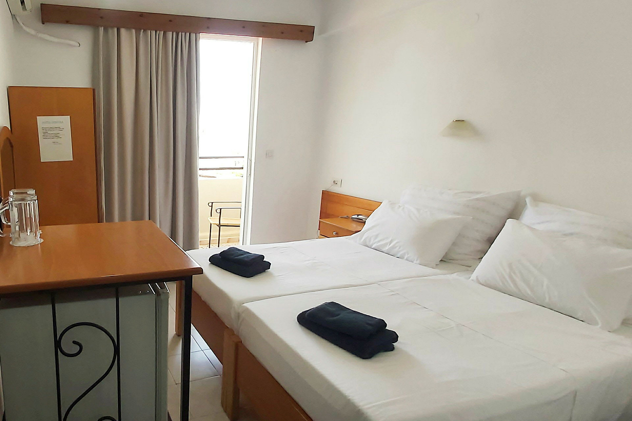 Ett hotellrum med två enkelsängar, en liten bordsskiva och en dörr som leder till balkongen. (AI-genererad text)