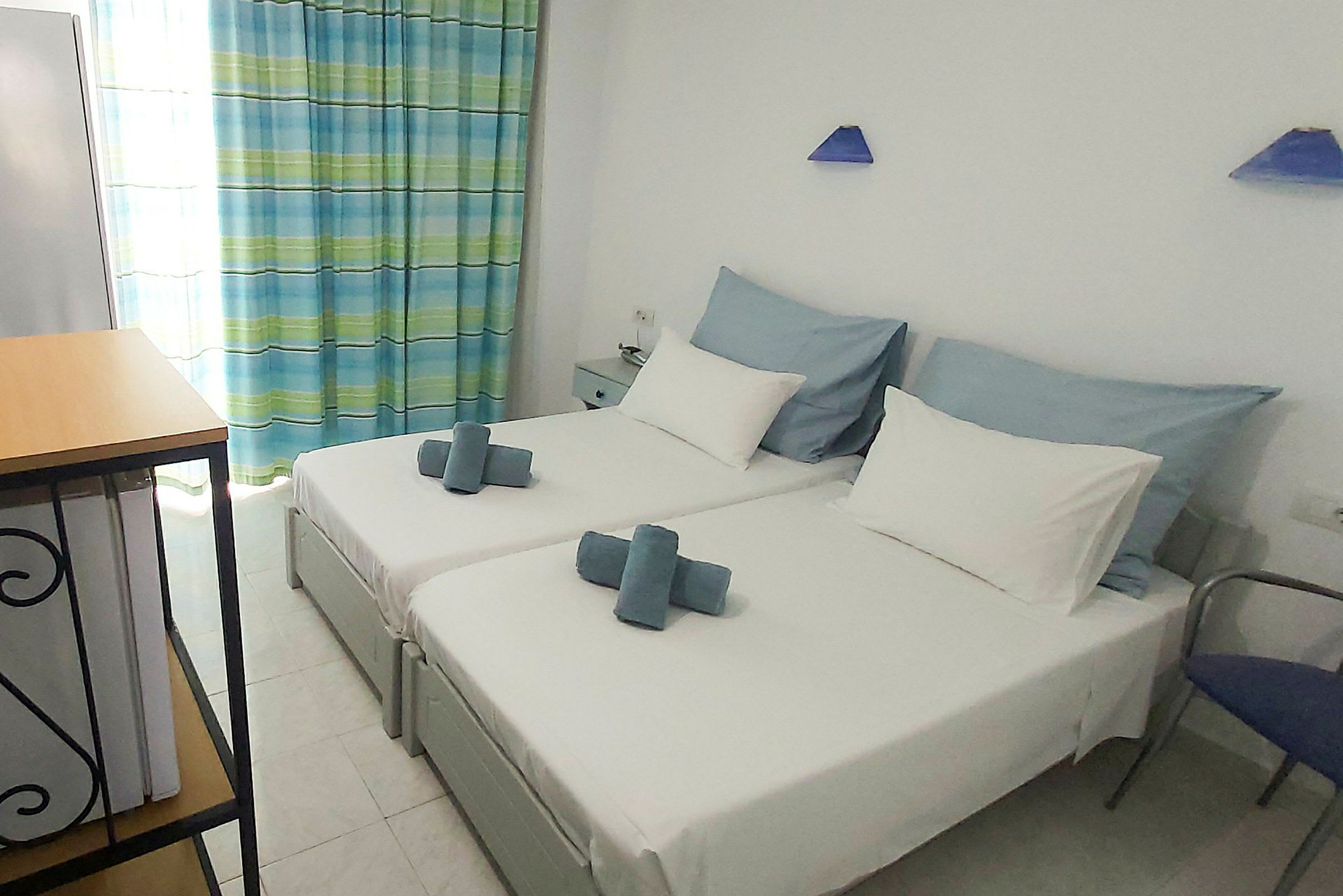 Bild av ett hotellrum med två enkelsängar, vit sängklädsel och blå dekoration. (AI-genererad text)