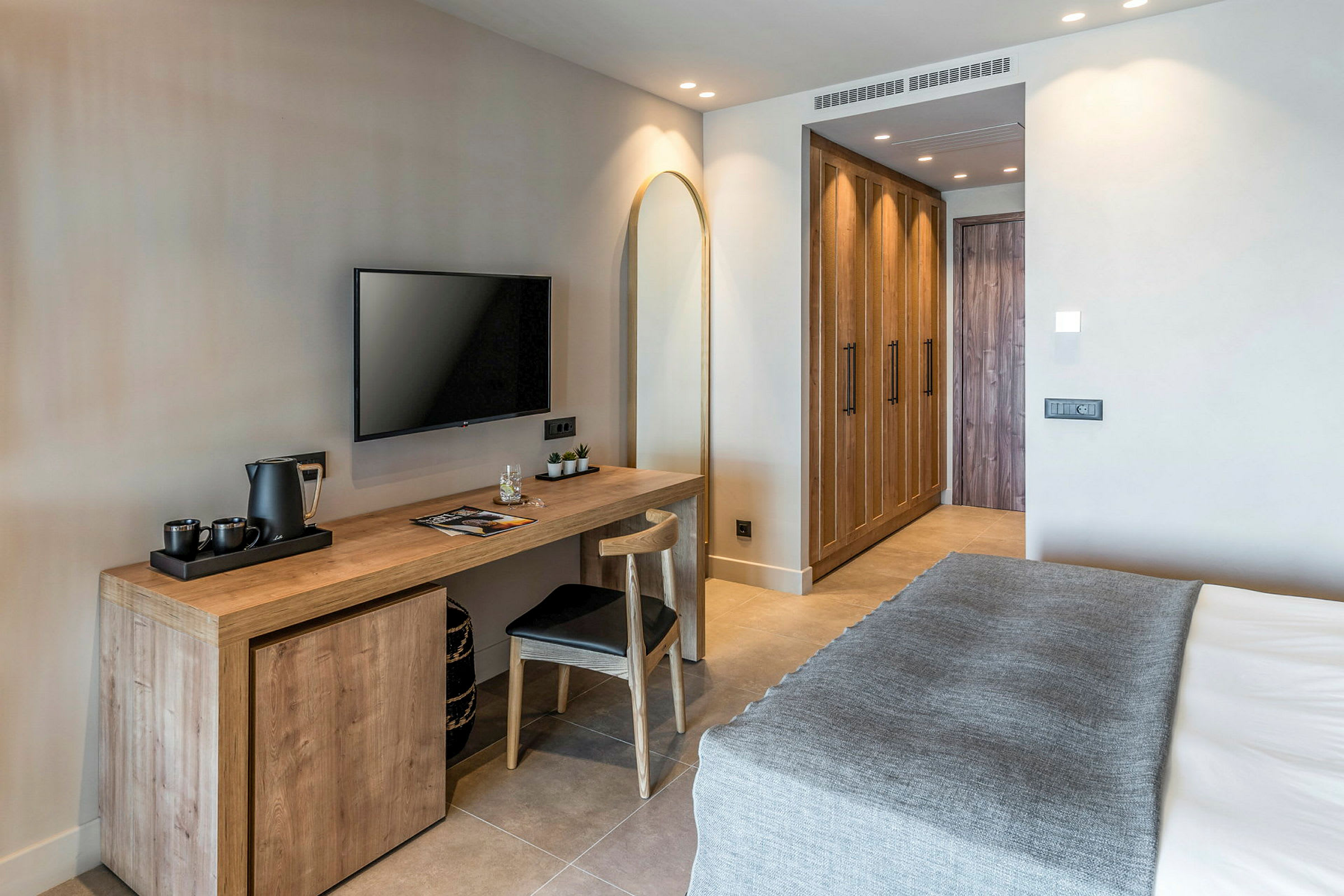 Ett modernt hotellrum med en säng, skrivbord, stol, väggmonterad TV och garderober. (AI-genererad text)