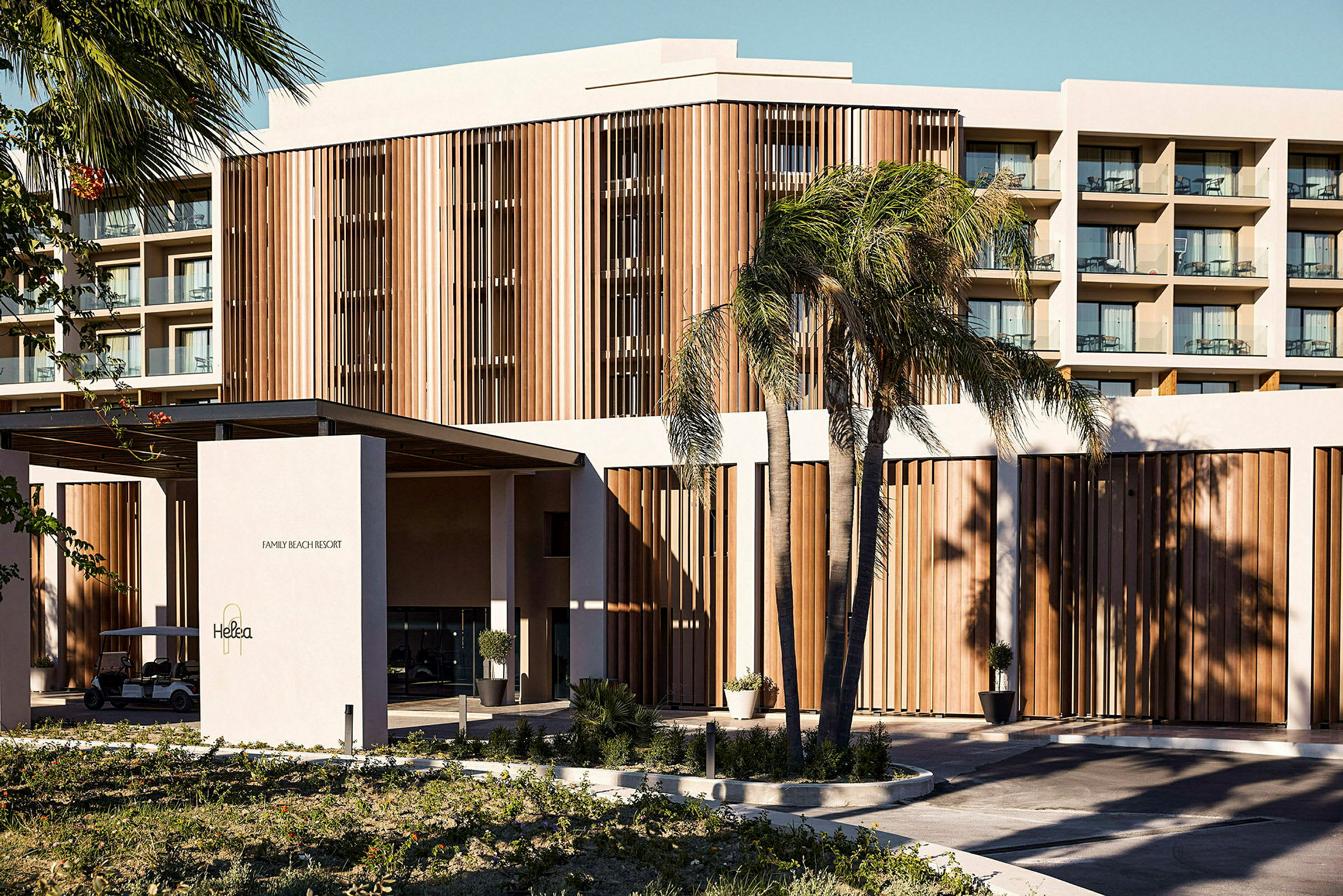 Ett hotell med en modern arkitektur och träpaneler, omgiven av palmer. (AI-genererad text)
