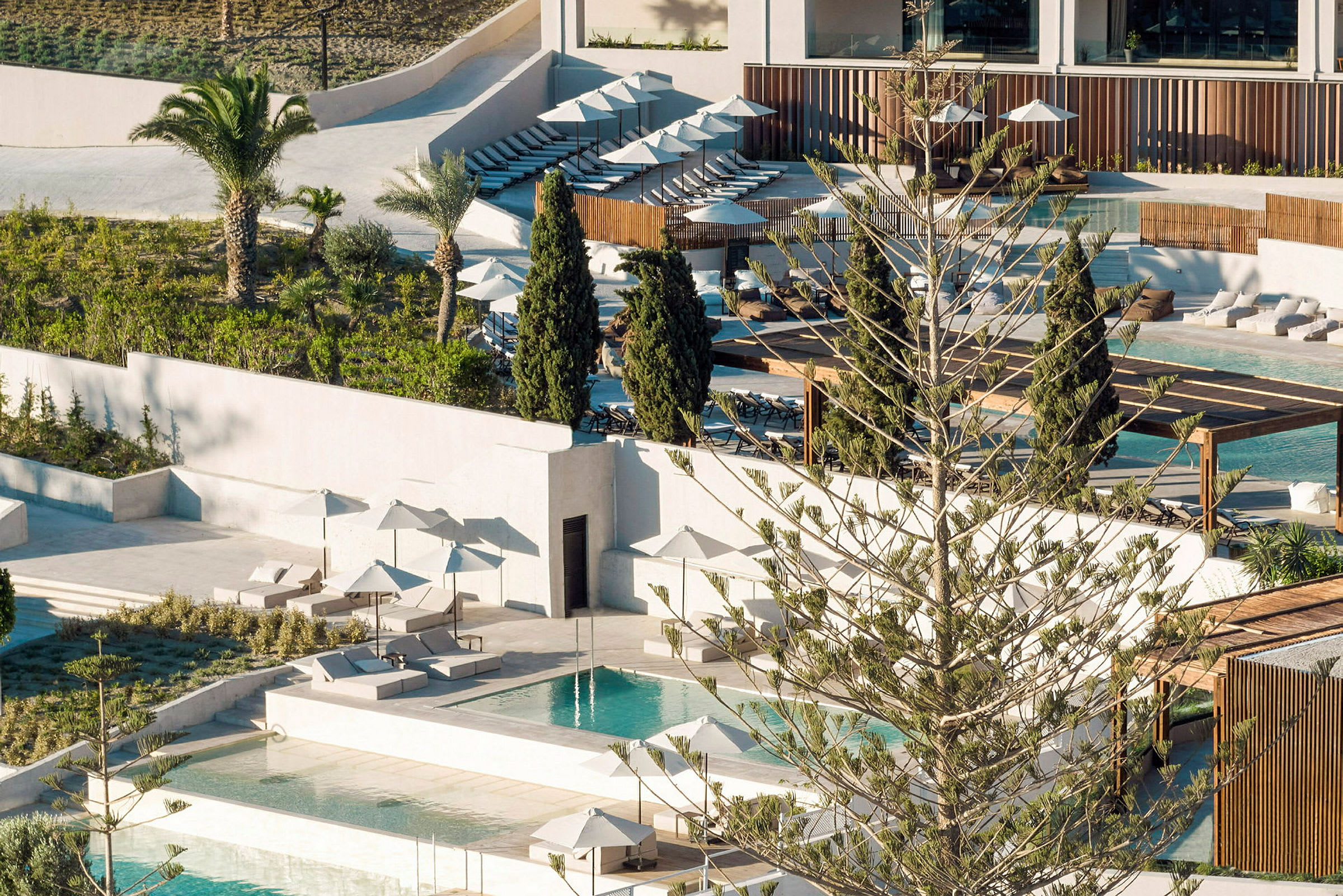 Vy över ett hotellområde med pooler, solsängar och parasoller, omgärdat av grönska. (AI-genererad text)
