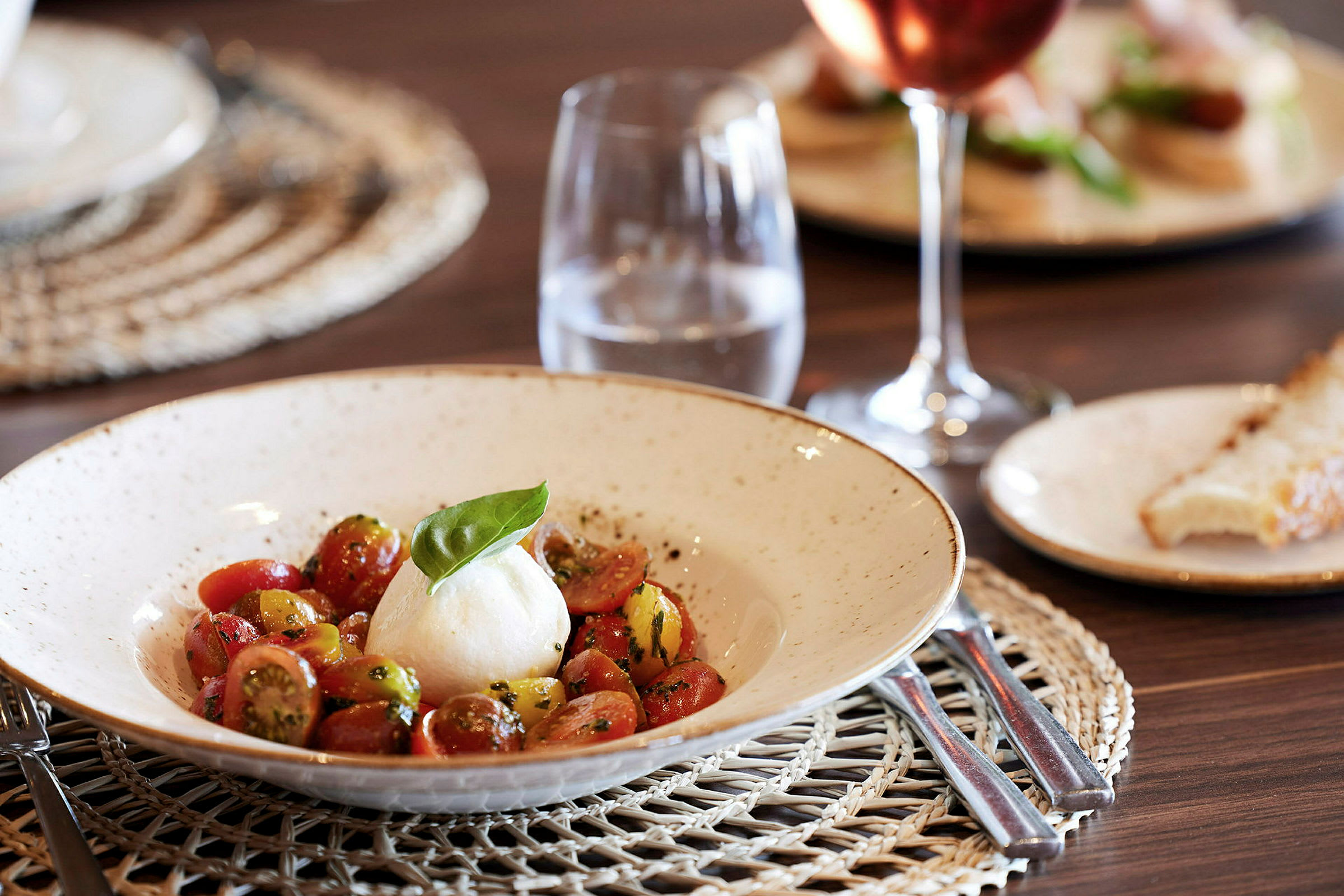 En tallrik med mozzarella och tomatsallad, samt ett glas vatten på ett bord. (AI-genererad text)