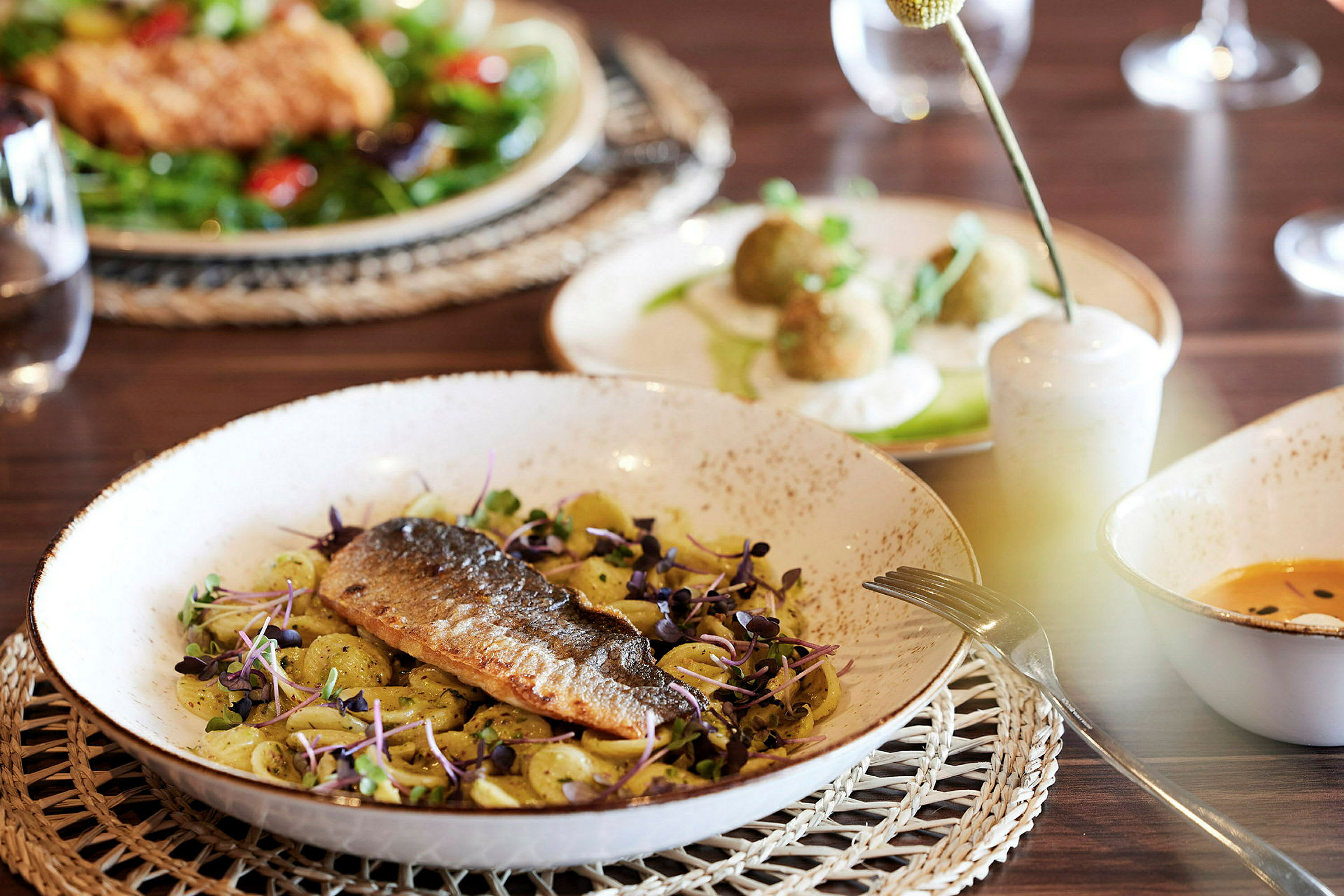 En tallrik med fisk och pasta, omgiven av andra rätter på ett bord. (AI-genererad text)