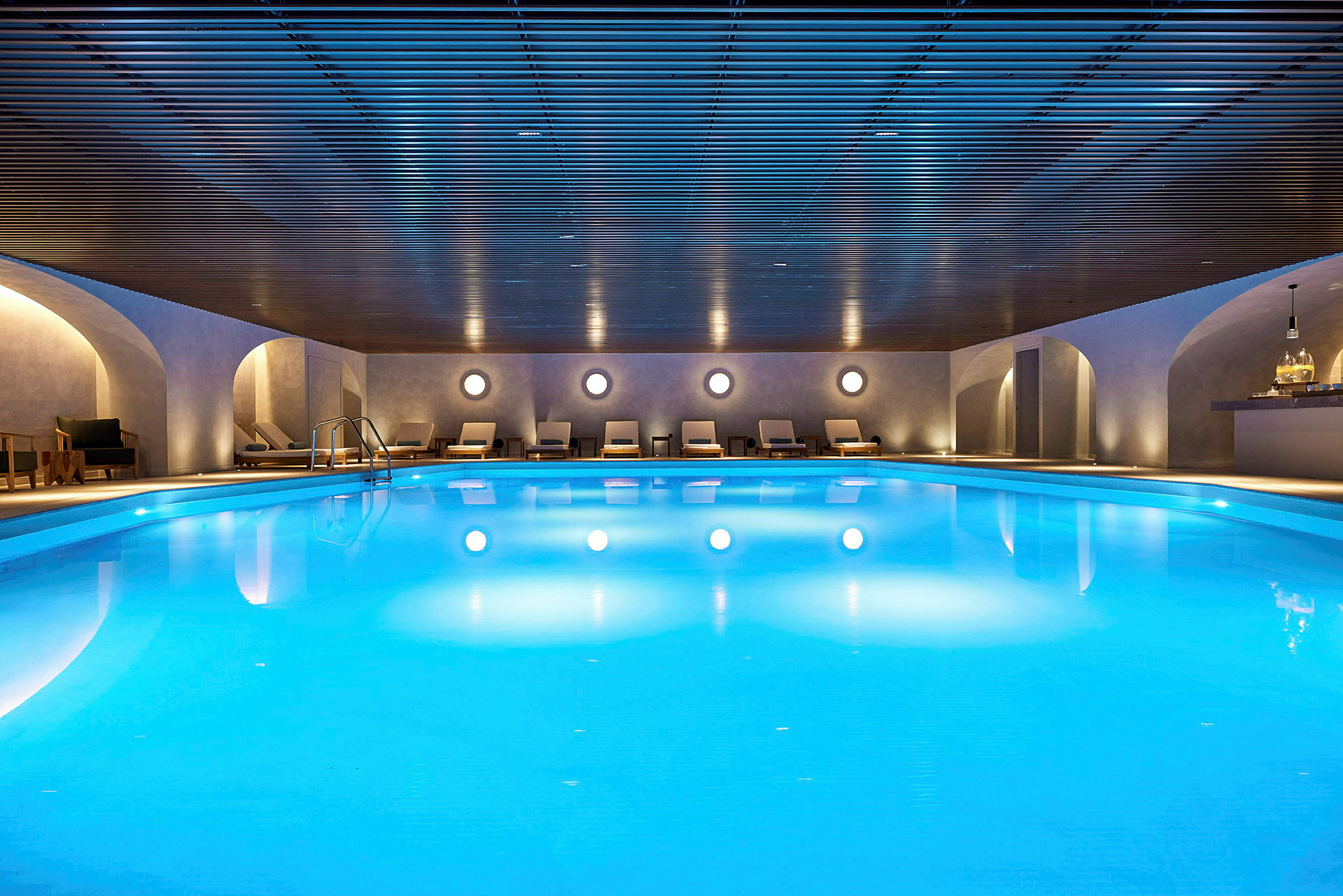 En inomhuspool med omgivande solstolar och en modern takdesign. (AI-genererad text)
